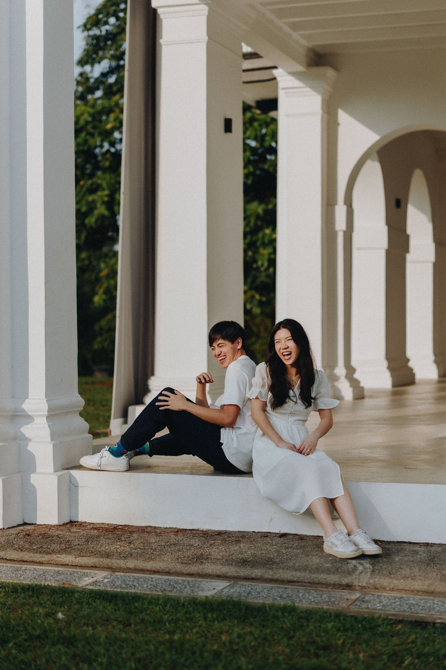 Couple relaxing on white columned porch in casual attire.