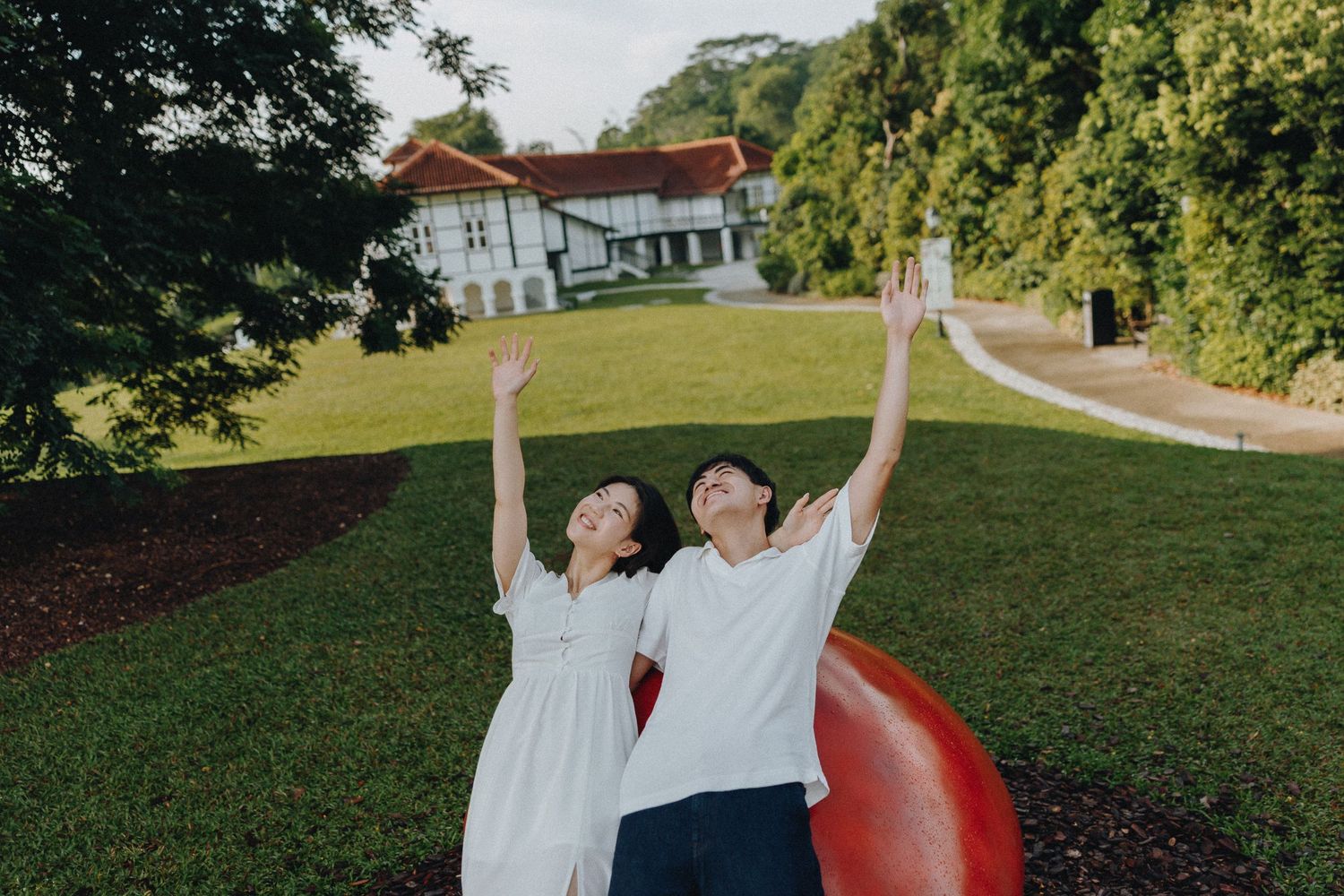 A couple jumps joyfully in a park setting with trees in the background.