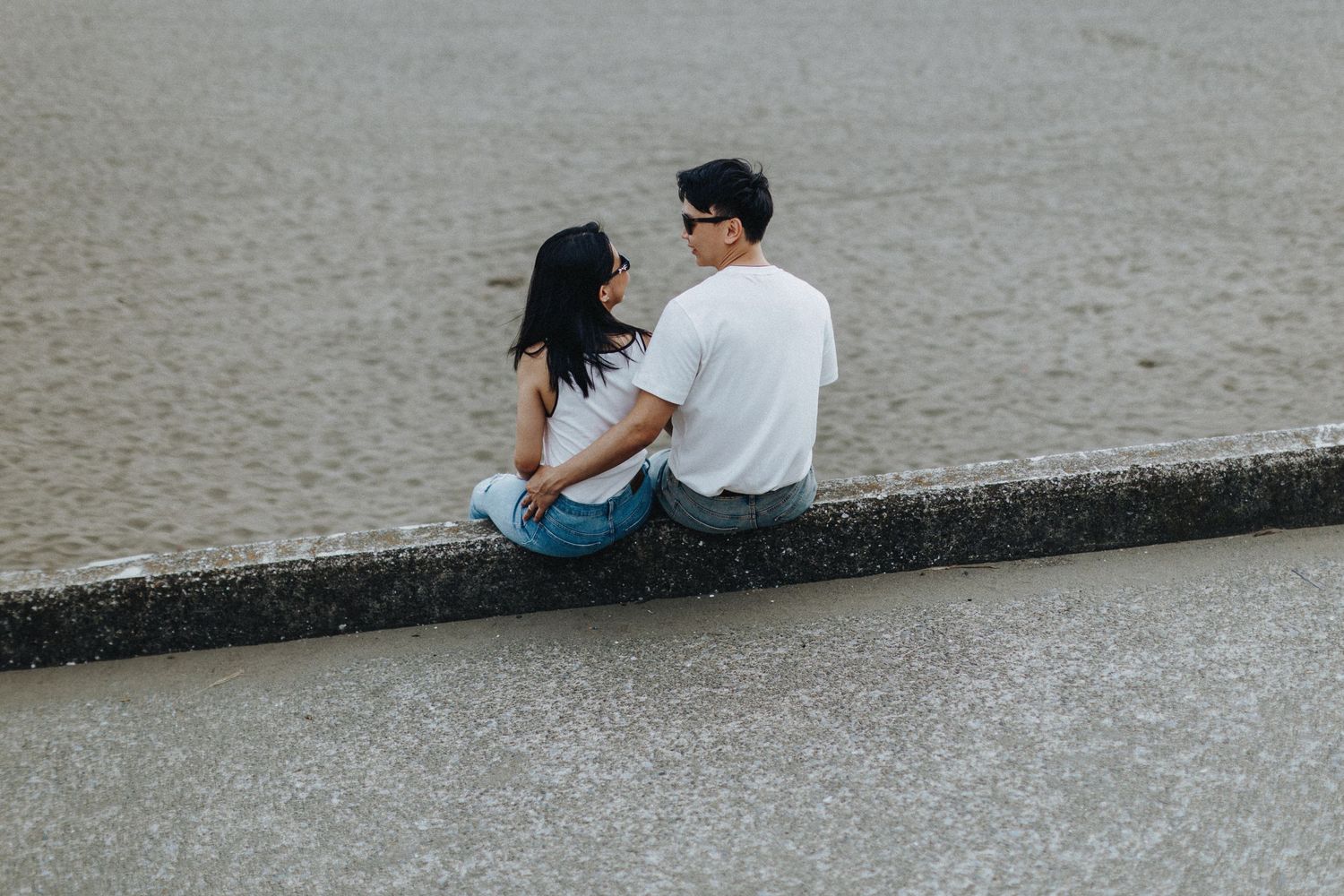 Couple sitting close together on a concrete wall overlooking water.