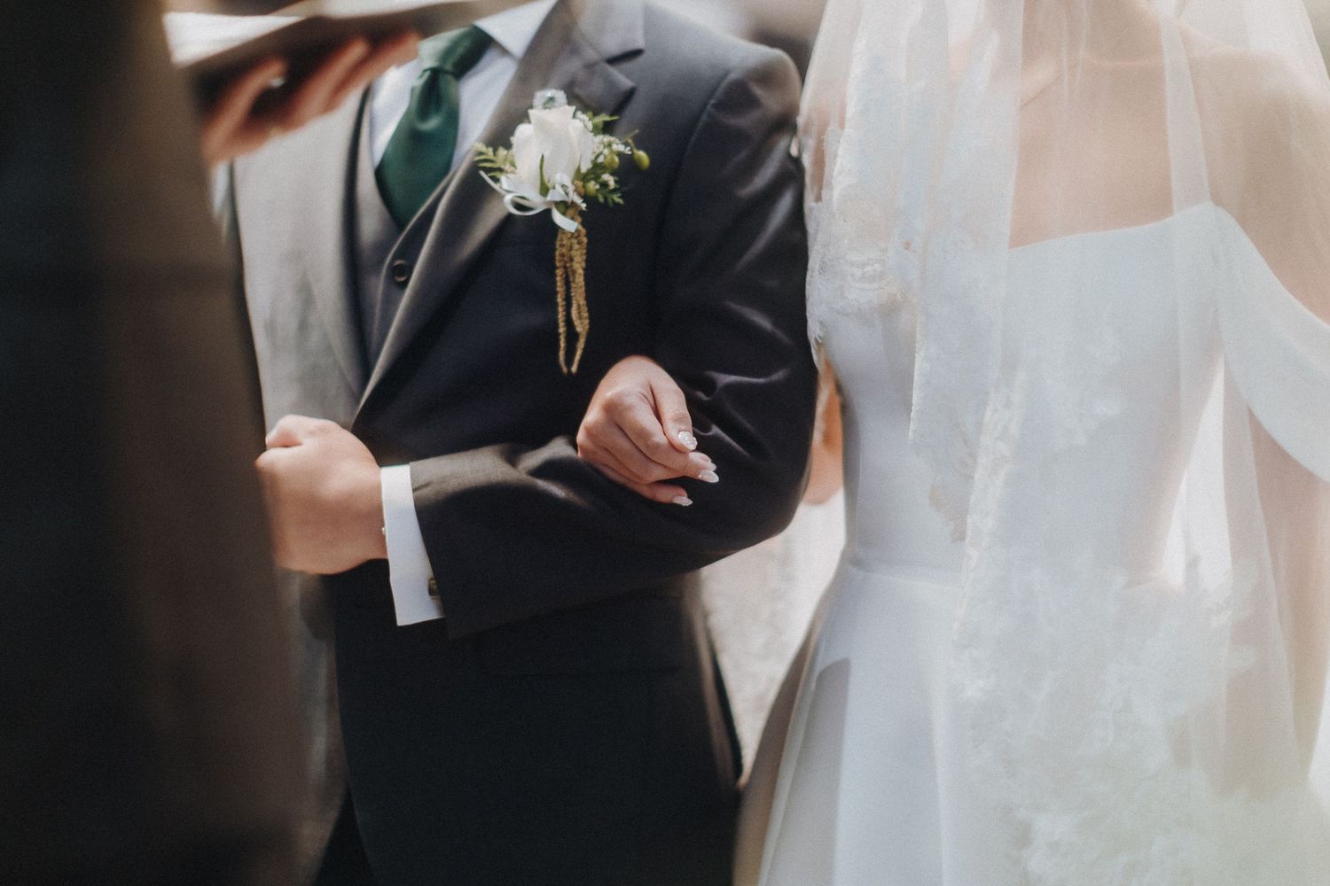 Close-up of hands during wedding ceremony with white boutonniere detail.