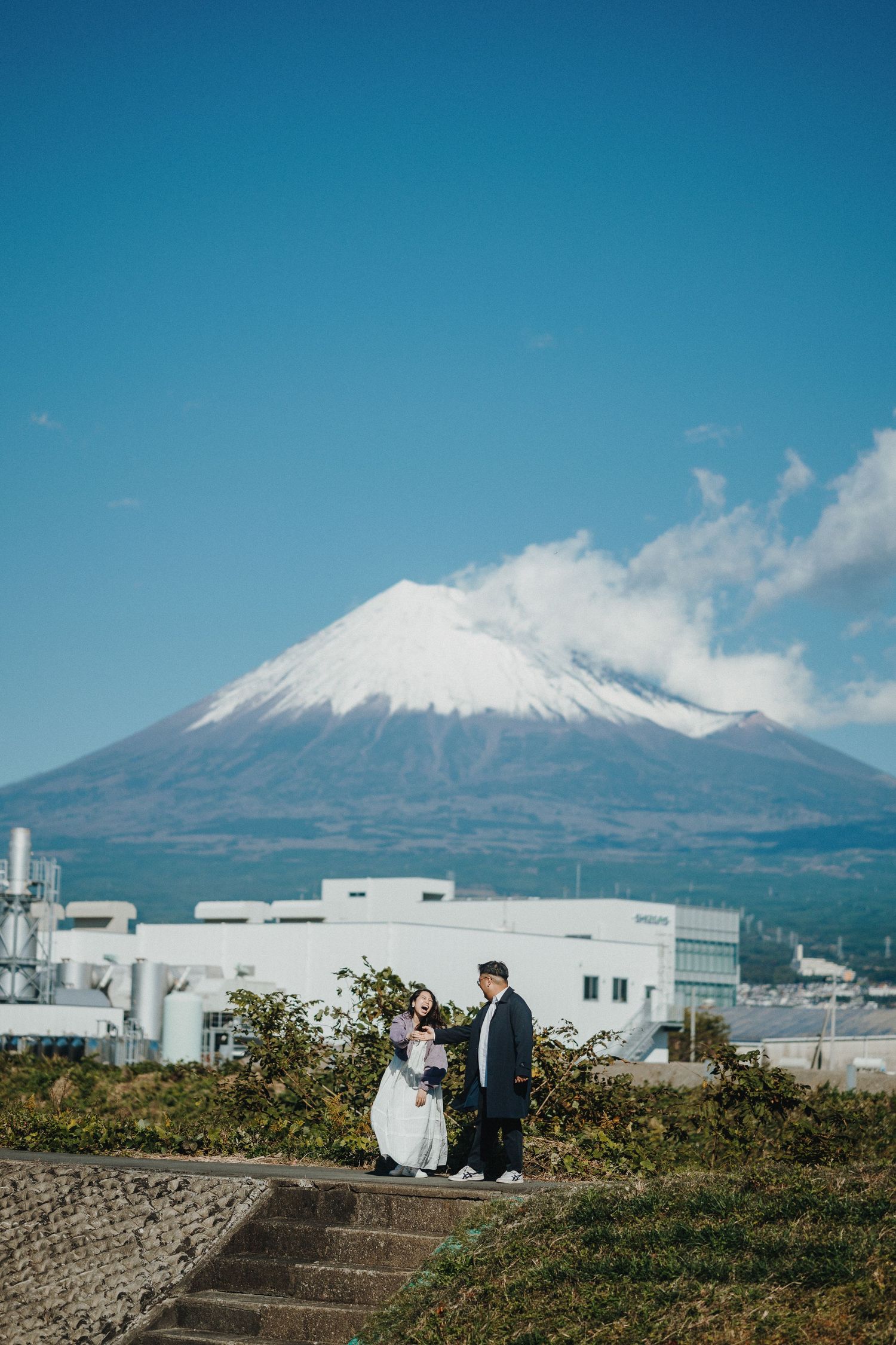 Snow-capped Mount Fuji rises majestically behind industrial buildings on a clear blue day.