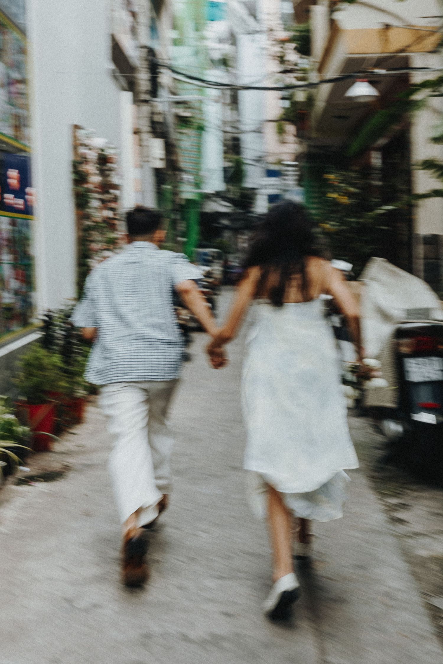 Couple running hand in hand down an urban alley in casual wedding attire.
