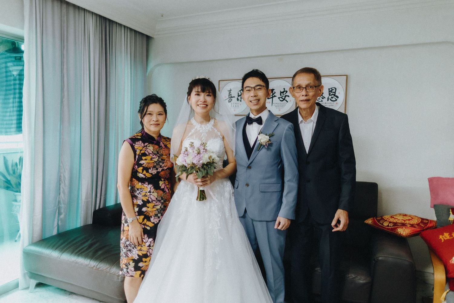 A formal wedding portrait taken in a bright living room with white curtains.
