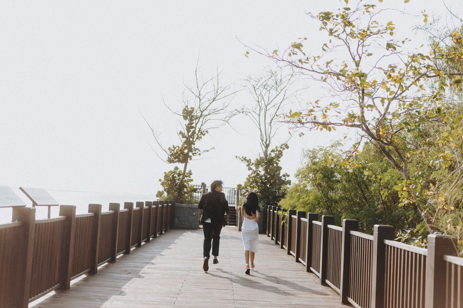 Two people walking together on a raised wooden boardwalk surrounded by autumn trees.