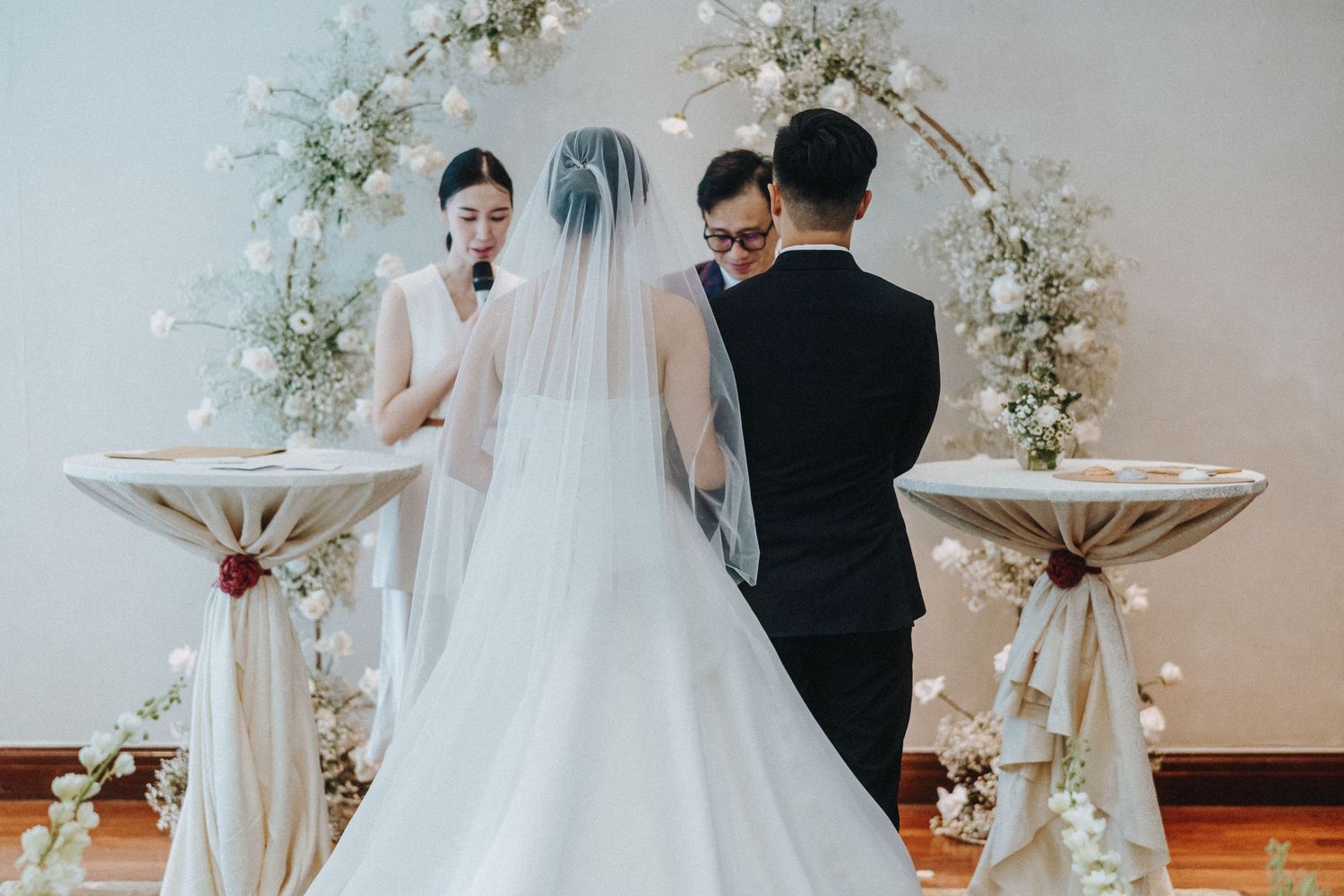Wedding ceremony setting with white floral arch and elegant decorations in a bright indoor space.