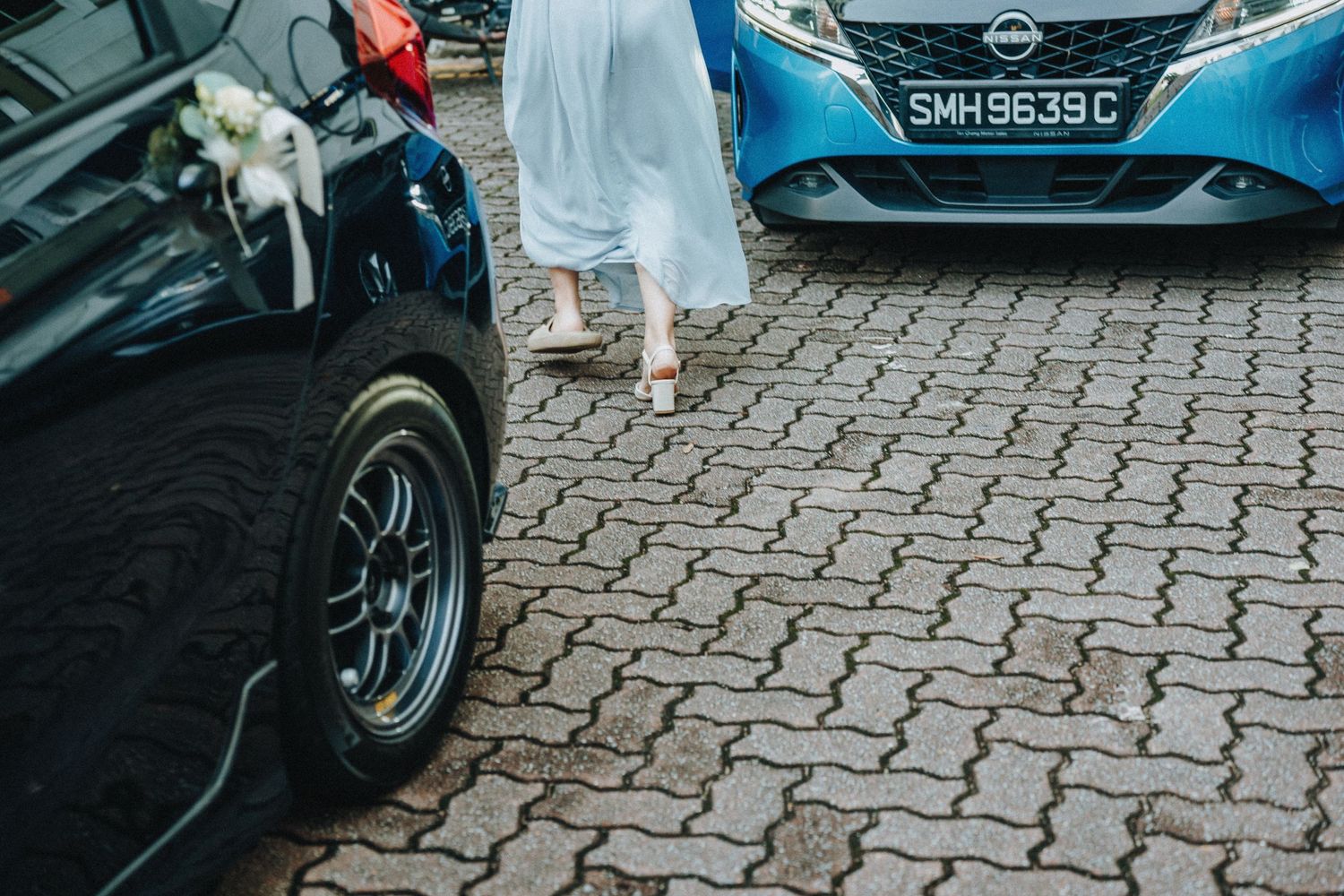 Cobblestone parking area with partial view of black and blue cars and white dress hem detail.