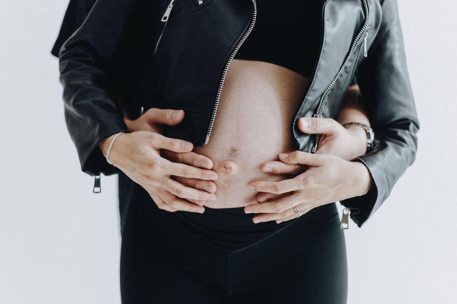 Close-up shot of hands tenderly cradling a pregnant belly while wearing a leather jacket.