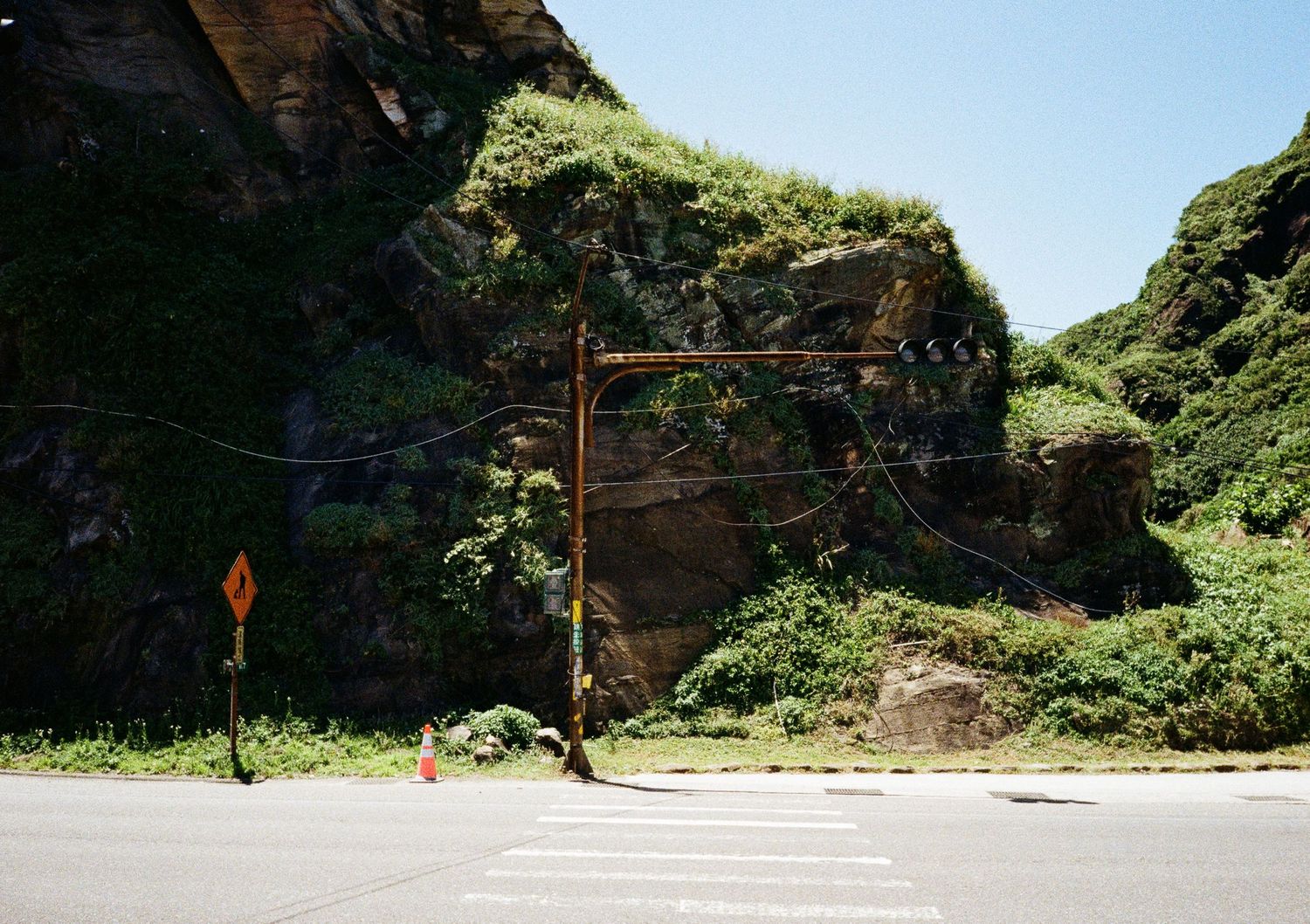 Empty mountain road curves through lush green cliffs.