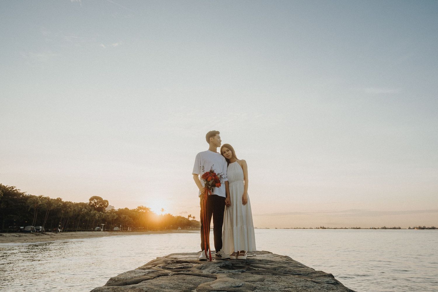 Couple standing together on a rocky beach overlook during golden hour sunset.