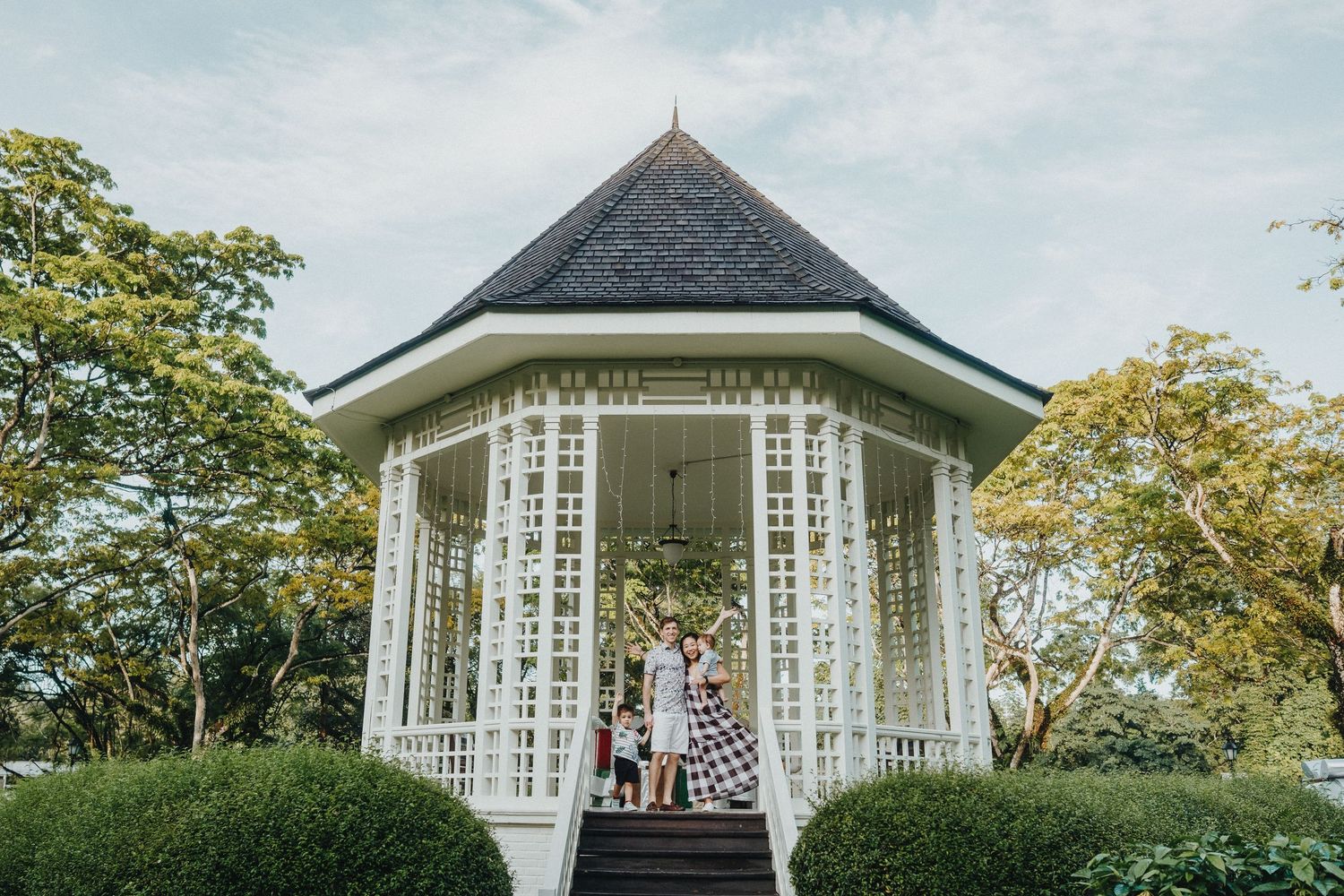 A white gazebo with elegant windows photographed from multiple angles against lush green garden landscaping.