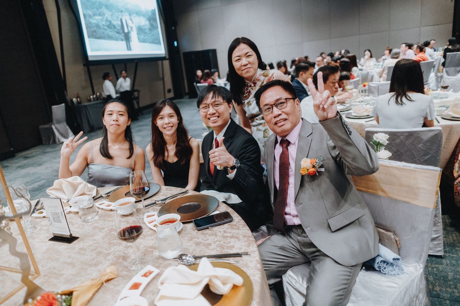 Wedding guests celebrate and pose for photos during a reception dinner in an elegant banquet hall.