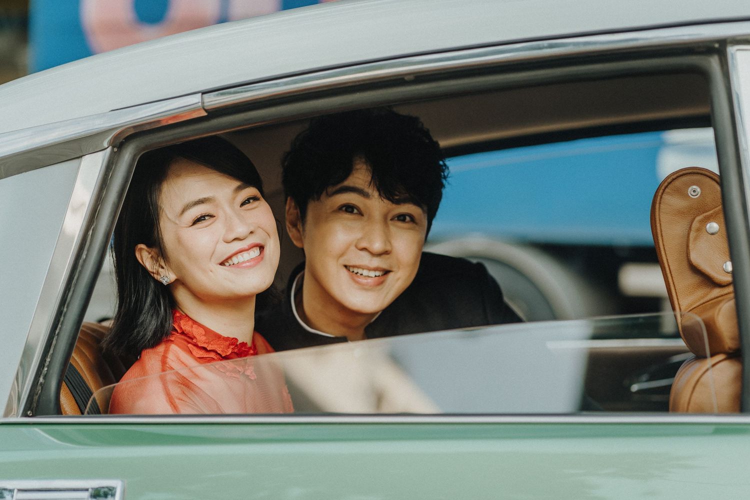 Joyful couple sharing laughter while seated in vintage mint green car.