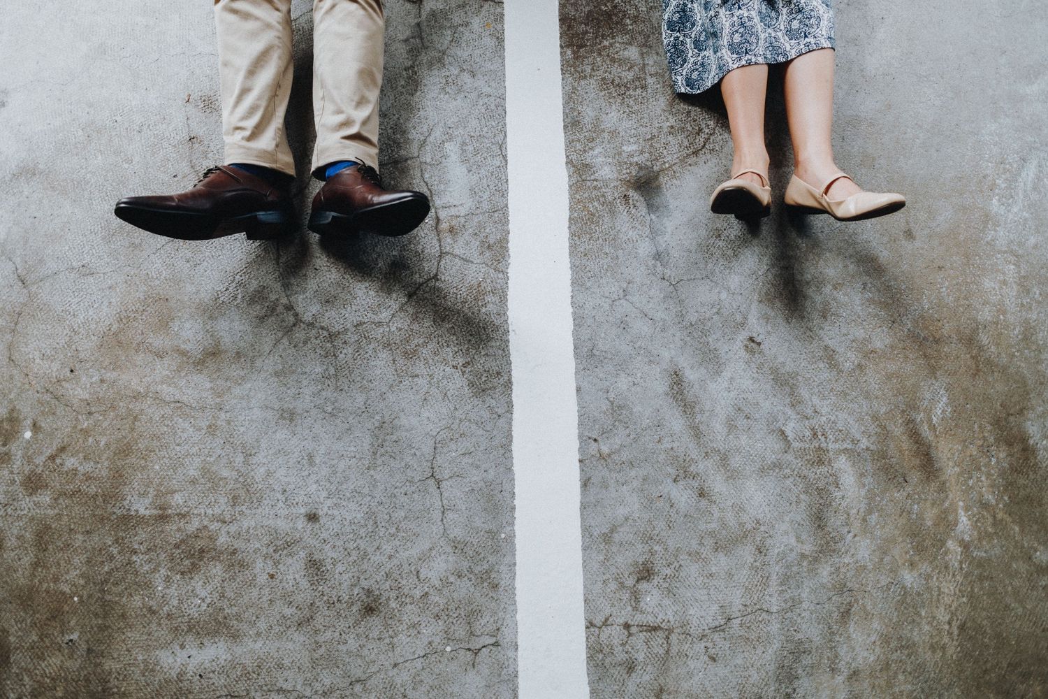 Two pairs of feet positioned on opposite sides of a white line on concrete ground.