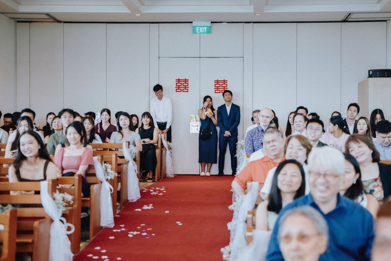Wedding ceremony aisle view with groom waiting at the altar as guests fill the decorated venue.