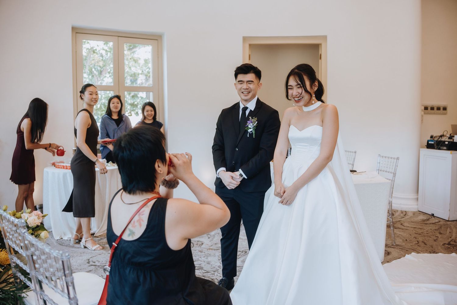 Bride in white gown and groom in black suit pose for photos with guests at wedding reception.