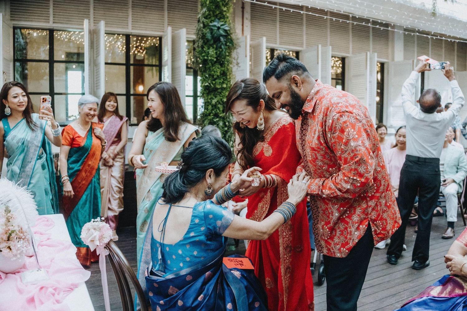 Guests in vibrant traditional attire celebrate at an Indian wedding ceremony with joyful interactions.