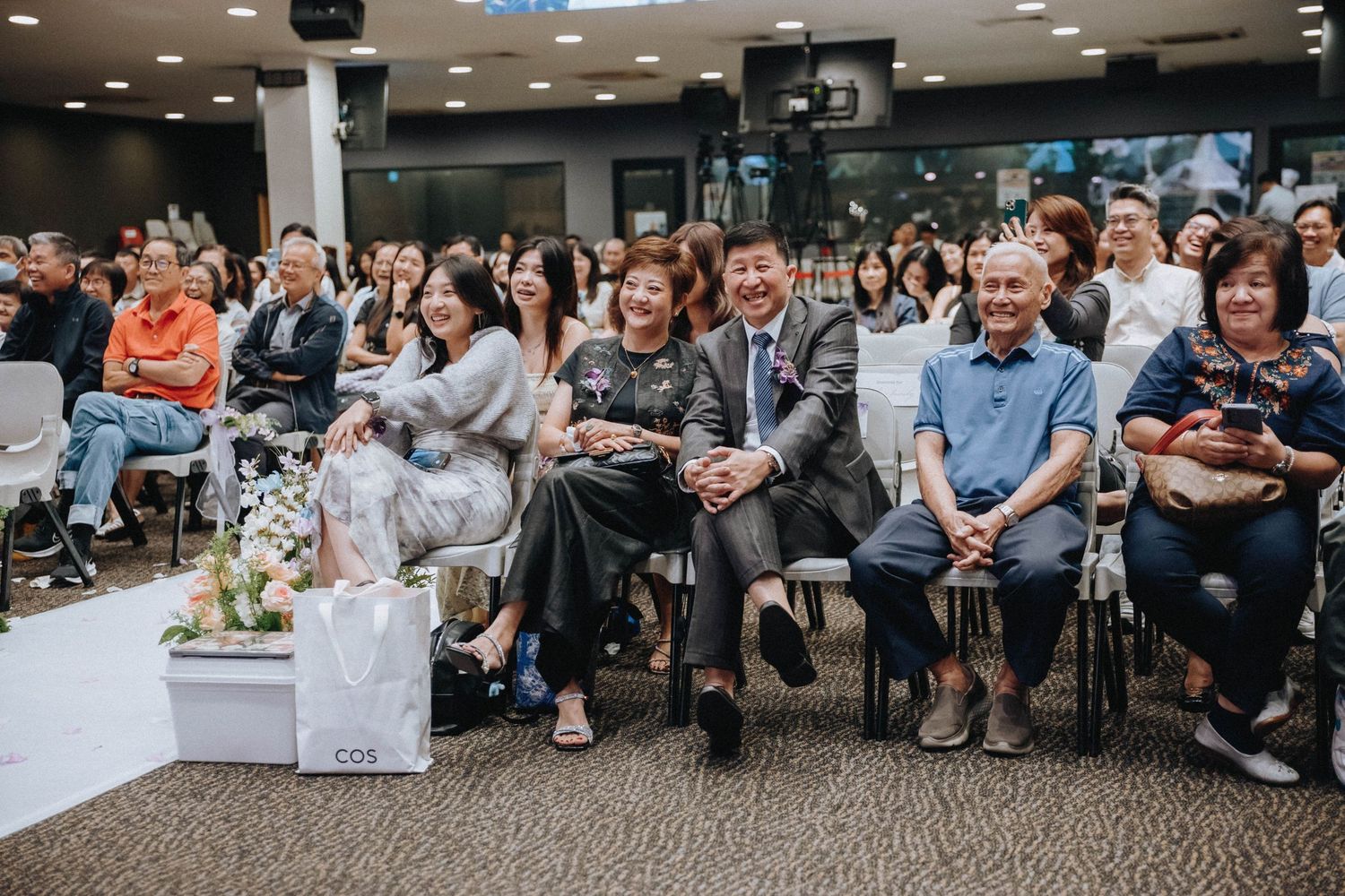 Wedding guests seated in rows watch the ceremony in an indoor venue with modern lighting.