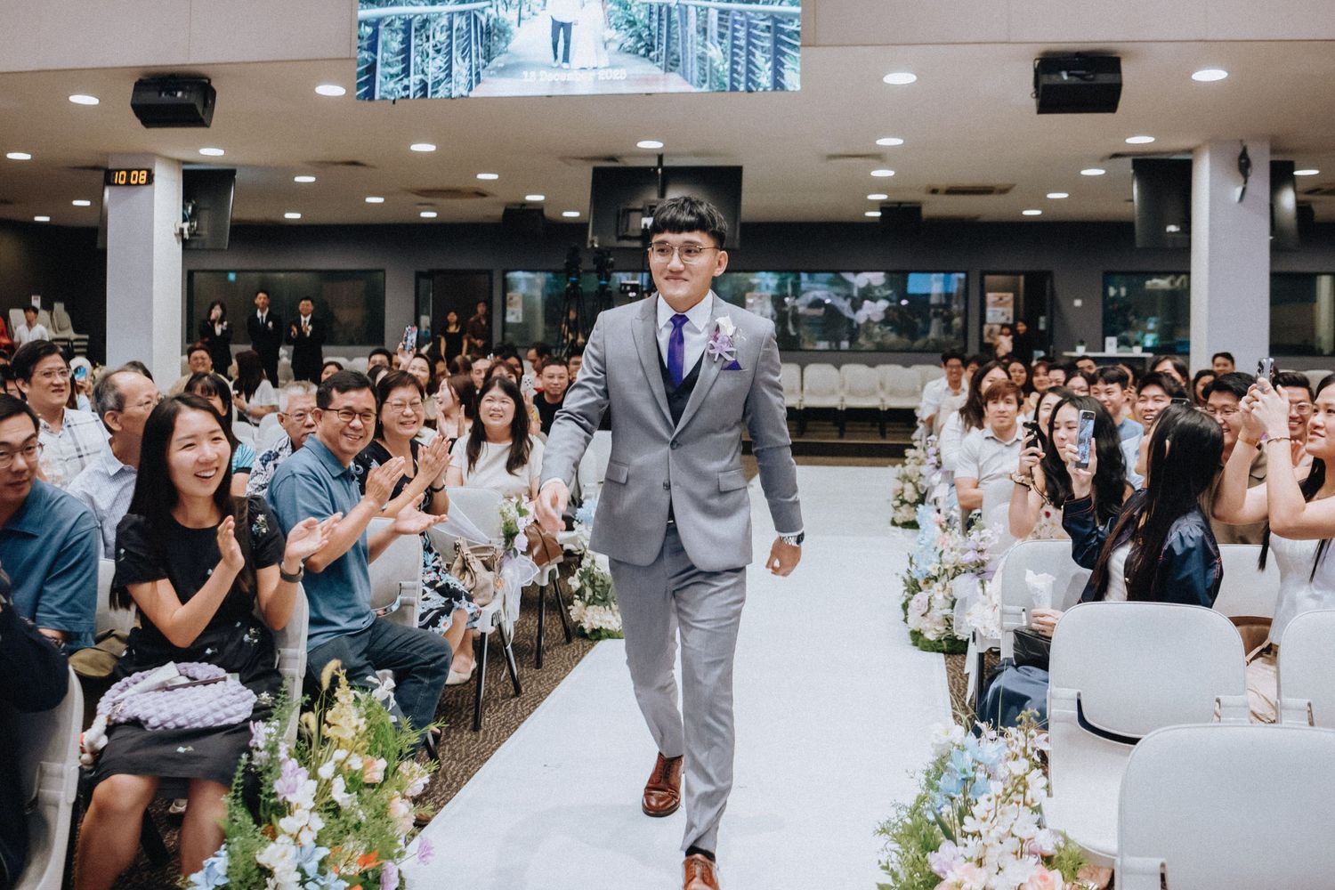 A decorated wedding aisle with white chairs and guests watching the ceremony.