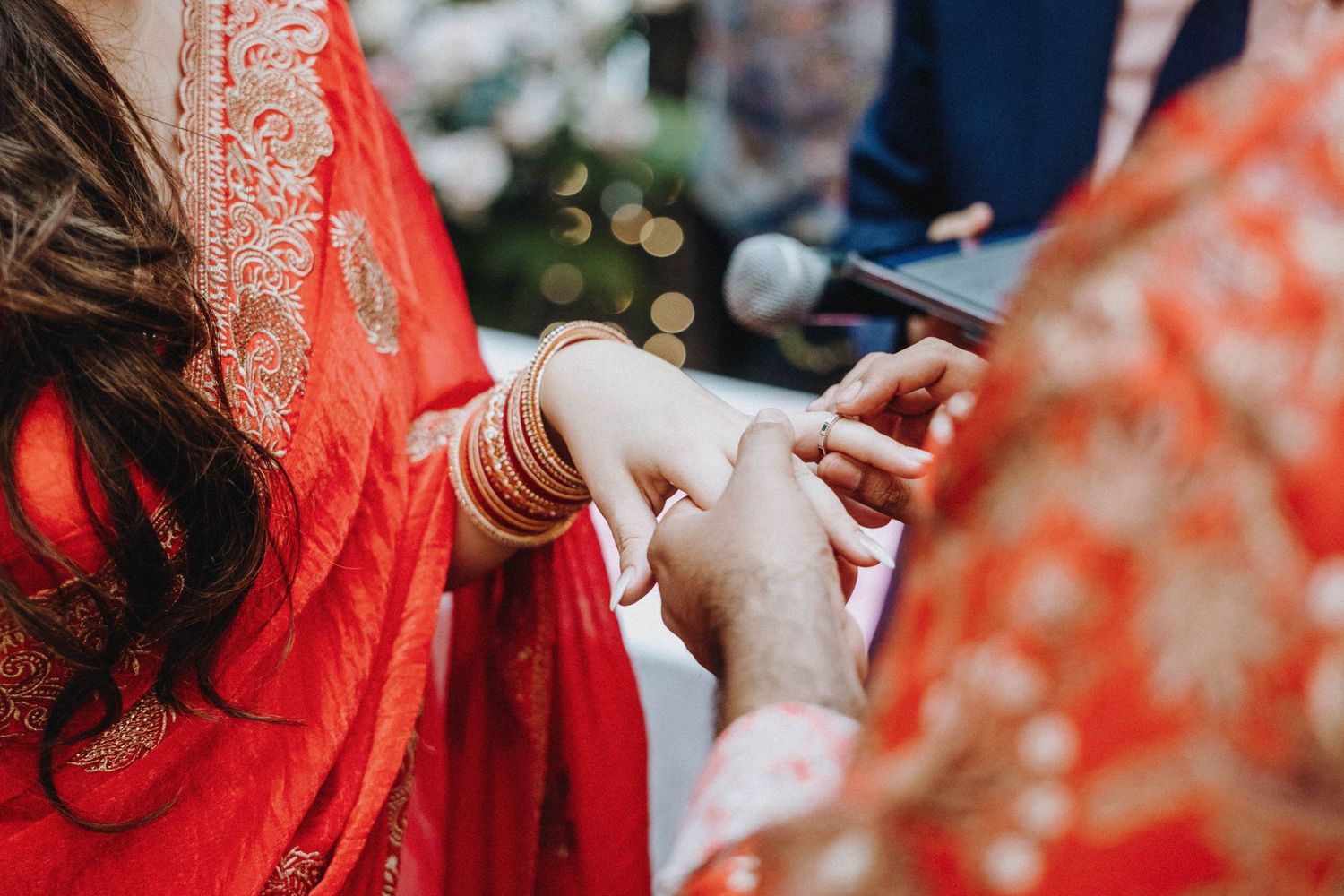 Close-up of Indian bride in red saree receiving ring during traditional wedding ceremony with gold bangles.