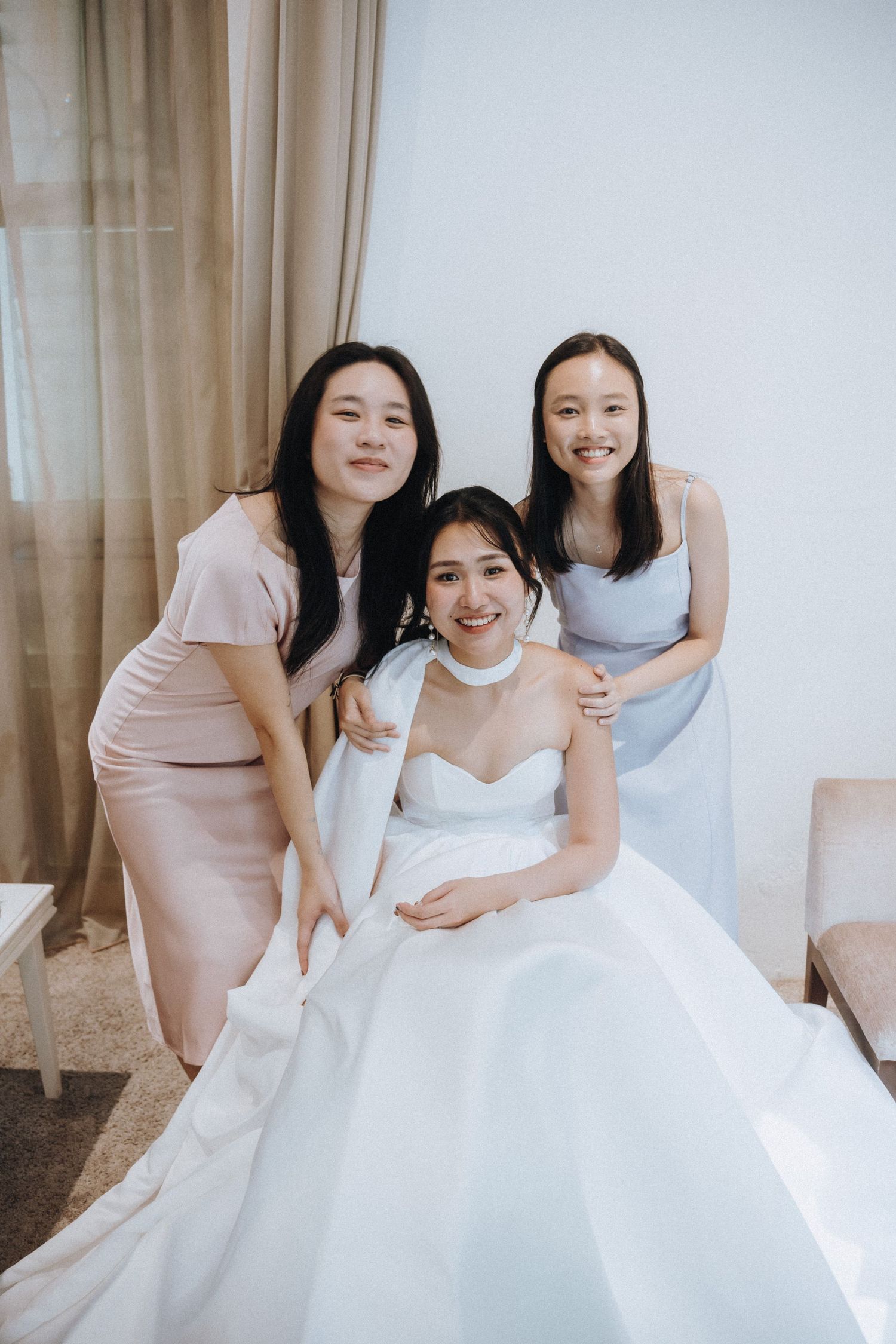Bride in white gown posing with two bridesmaids in pink and blue dresses.