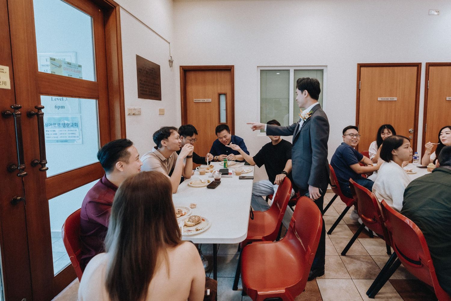 Groom stands and speaks to seated wedding guests at round tables during reception dinner.