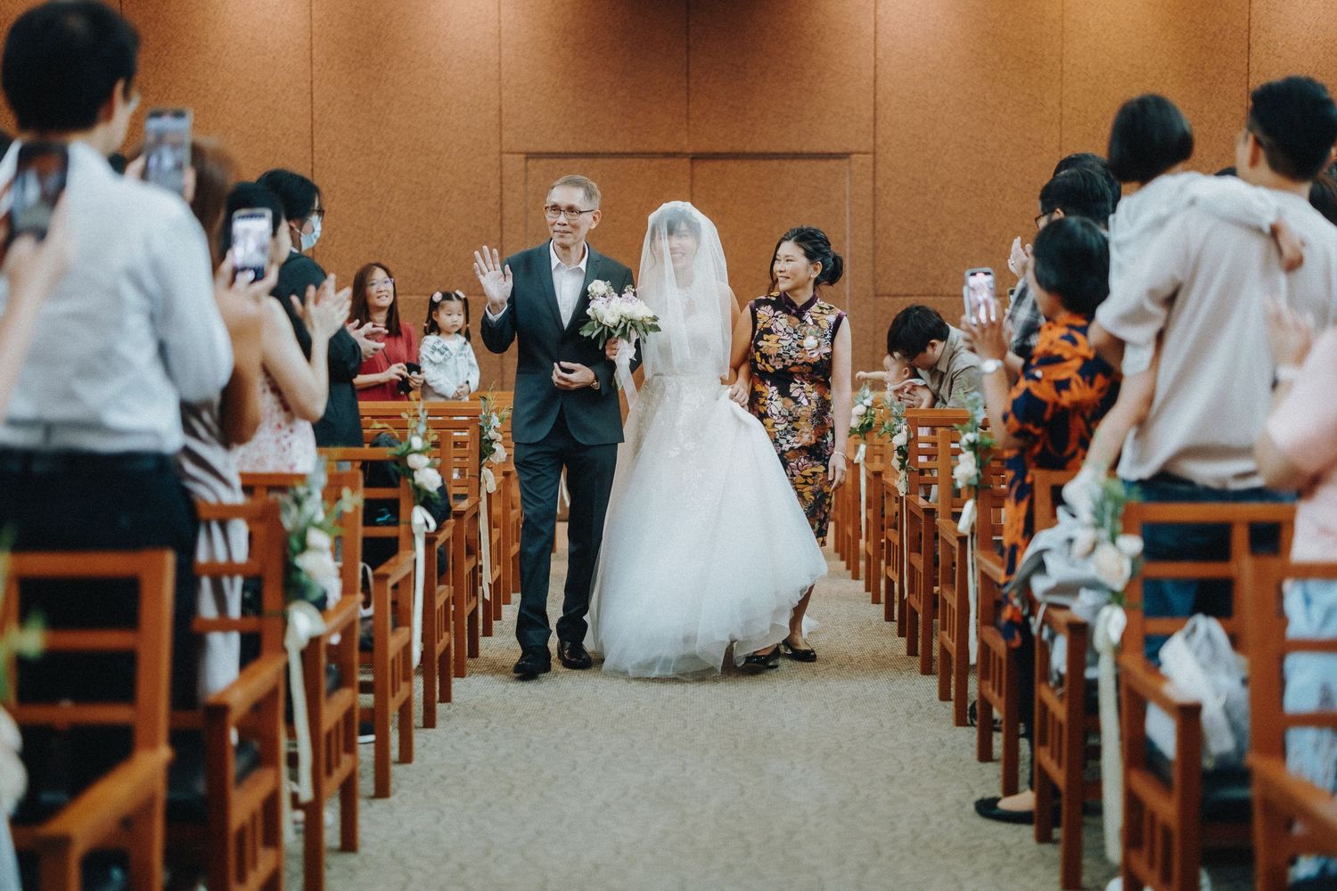 A wedding ceremony in progress inside a chapel with wooden pews and gathered attendees.