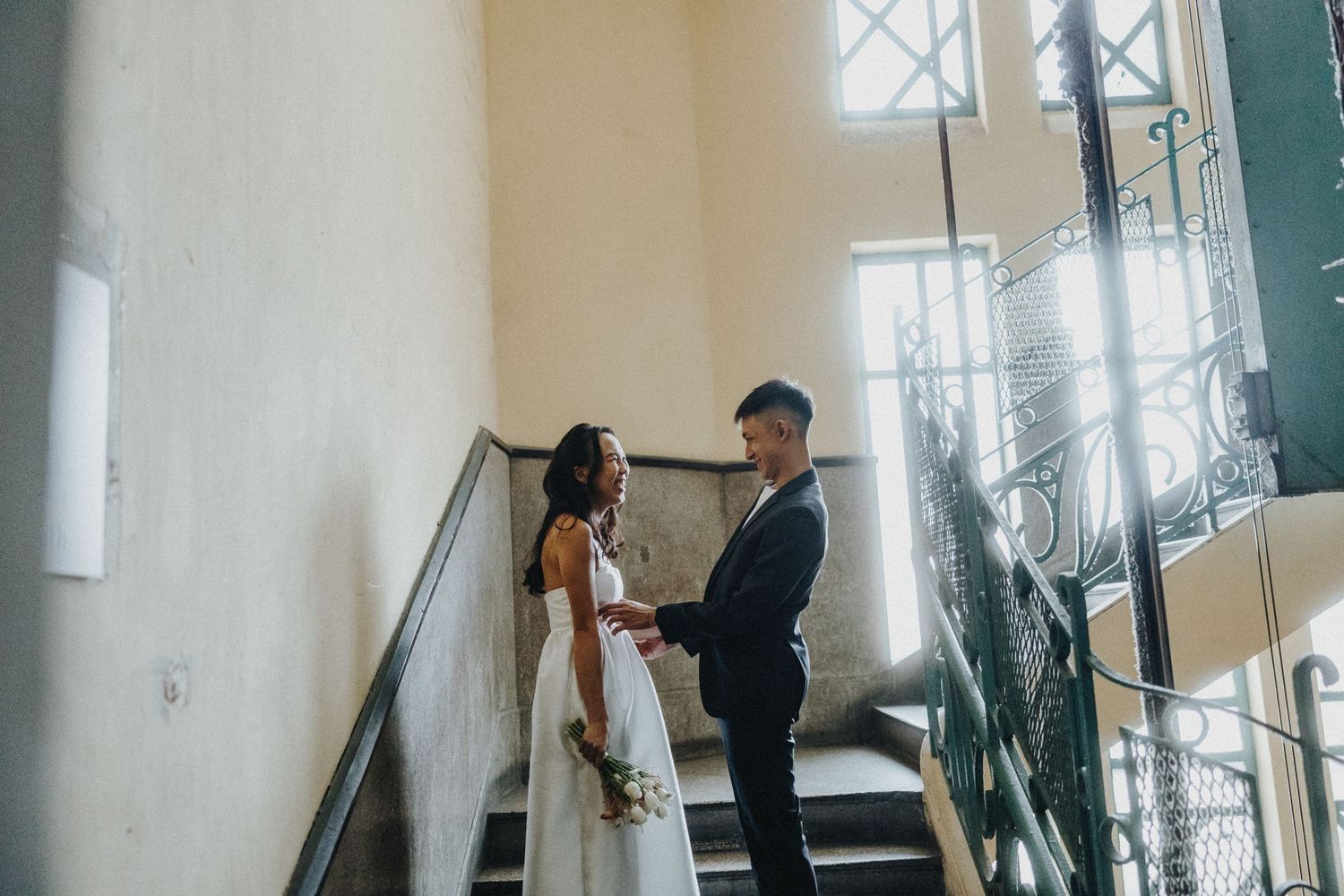A couple shares an intimate moment together on a staircase with natural light streaming through a window above.