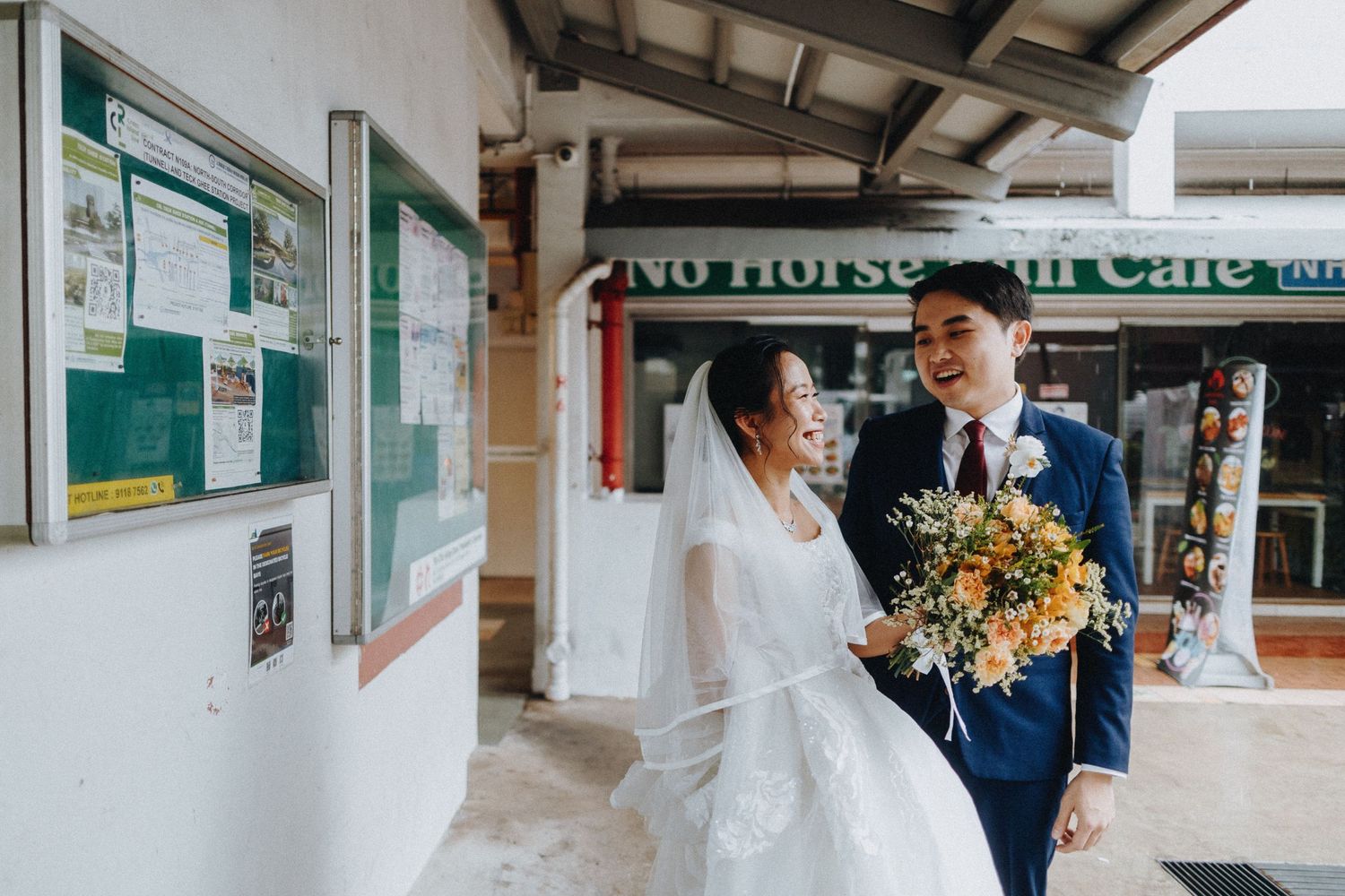 A wedding party walking together through a bright covered walkway with white columns and shopping storefronts.