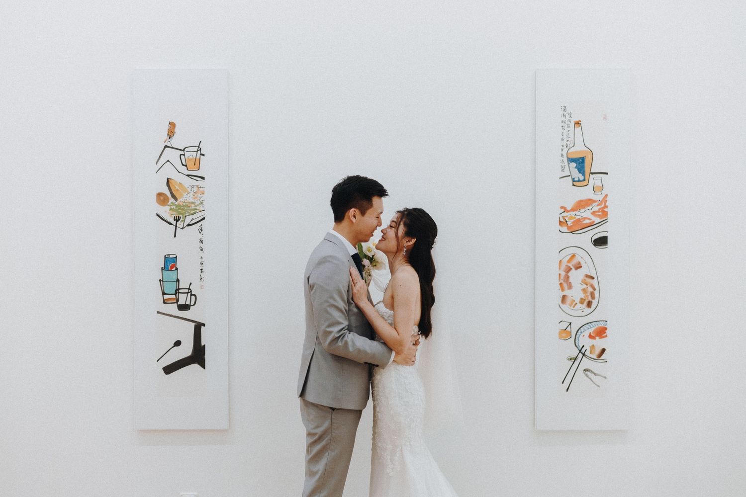 Two people in wedding attire embrace lovingly while surrounded by framed artwork in a gallery setting.