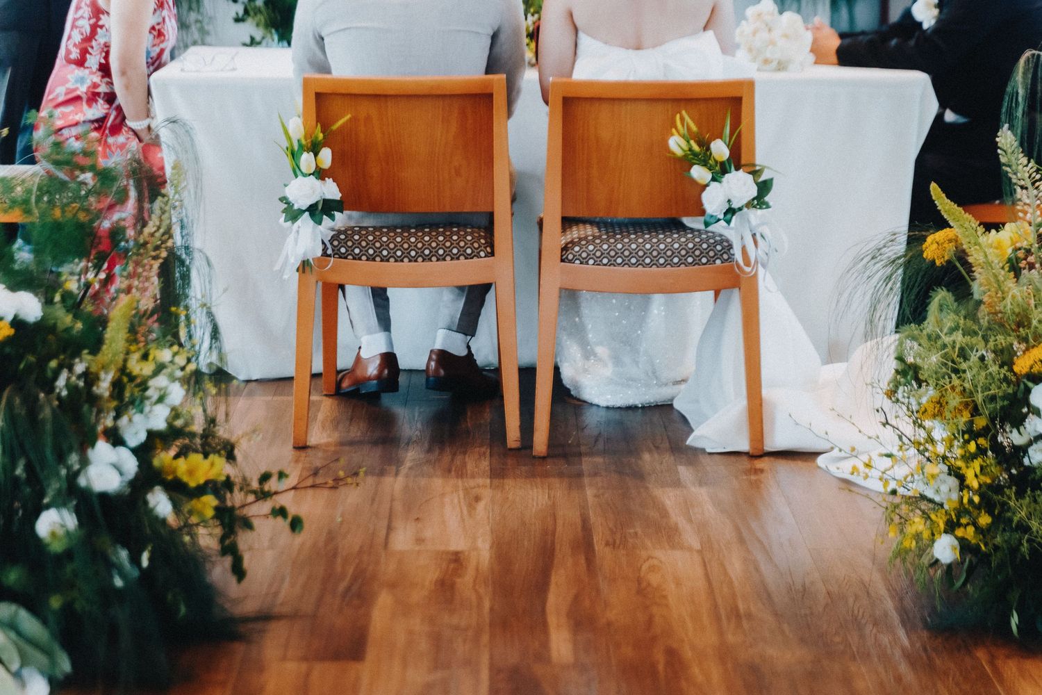 Wedding ceremony setup with wooden chairs and bright yellow floral arrangements in an indoor venue.