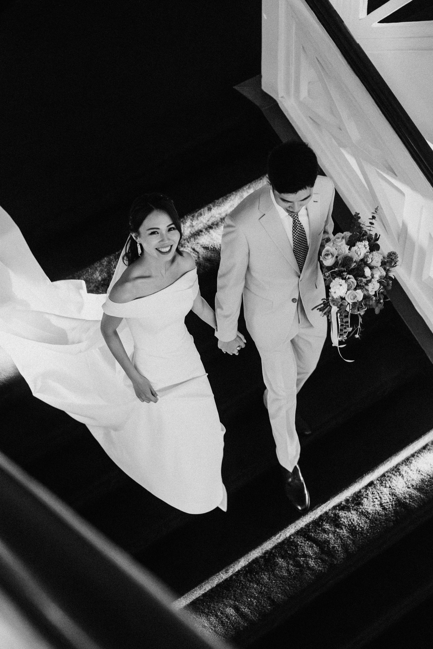 Black and white wedding photo series showing couple walking down stairs in dramatic light contrast and angles.