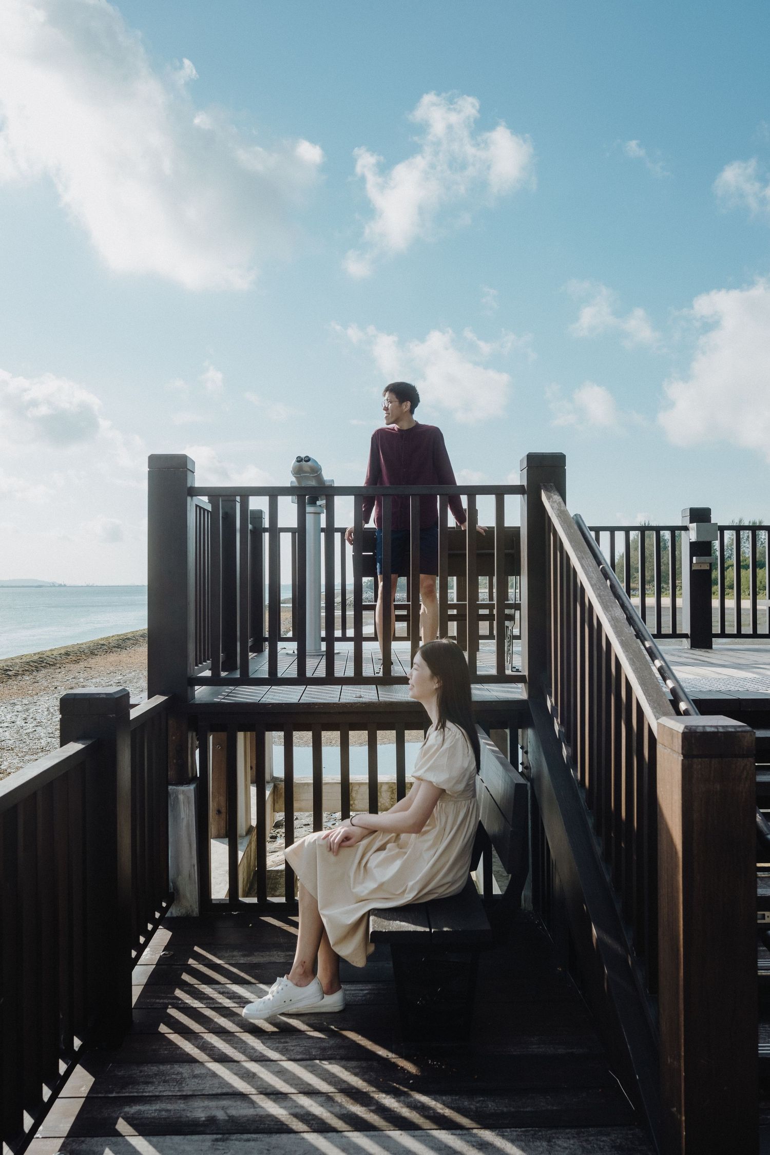 Two people share a peaceful moment on a wooden deck overlooking the ocean on a bright sunny day.