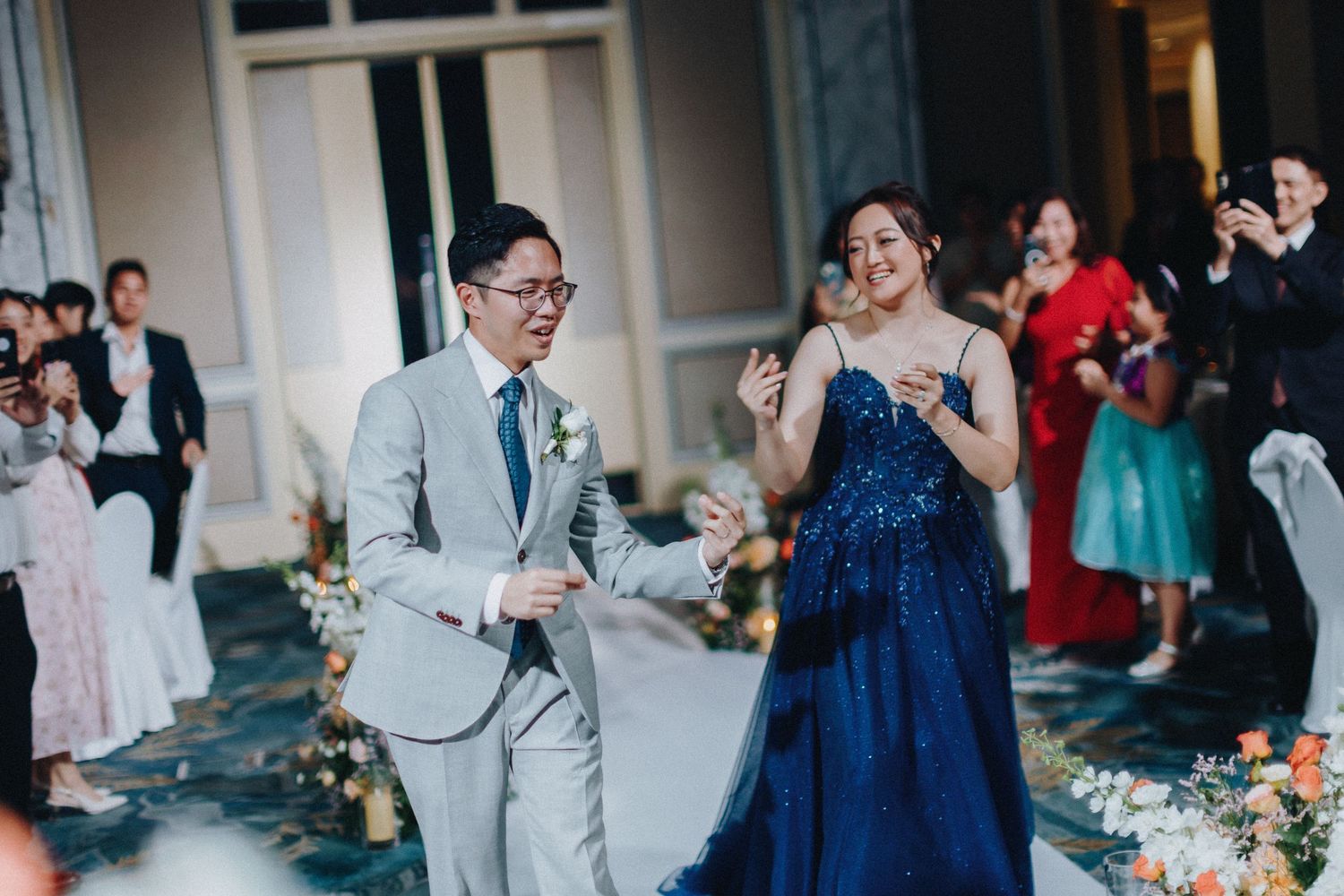 Wedding reception with guests in navy blue and gray attire mingling at decorated tables.