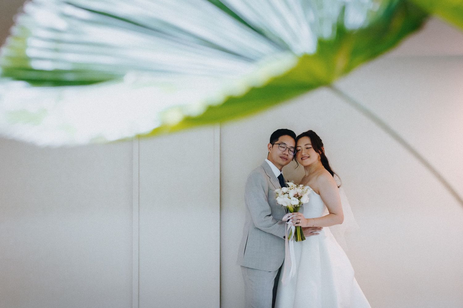 Elegant wedding couple poses against a white wall in a romantic portrait session.