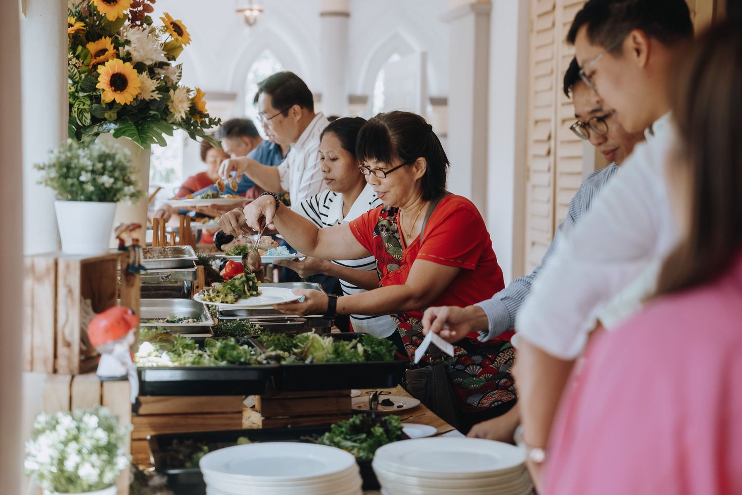 Wedding guests serving themselves at an outdoor buffet decorated with sunflowers.