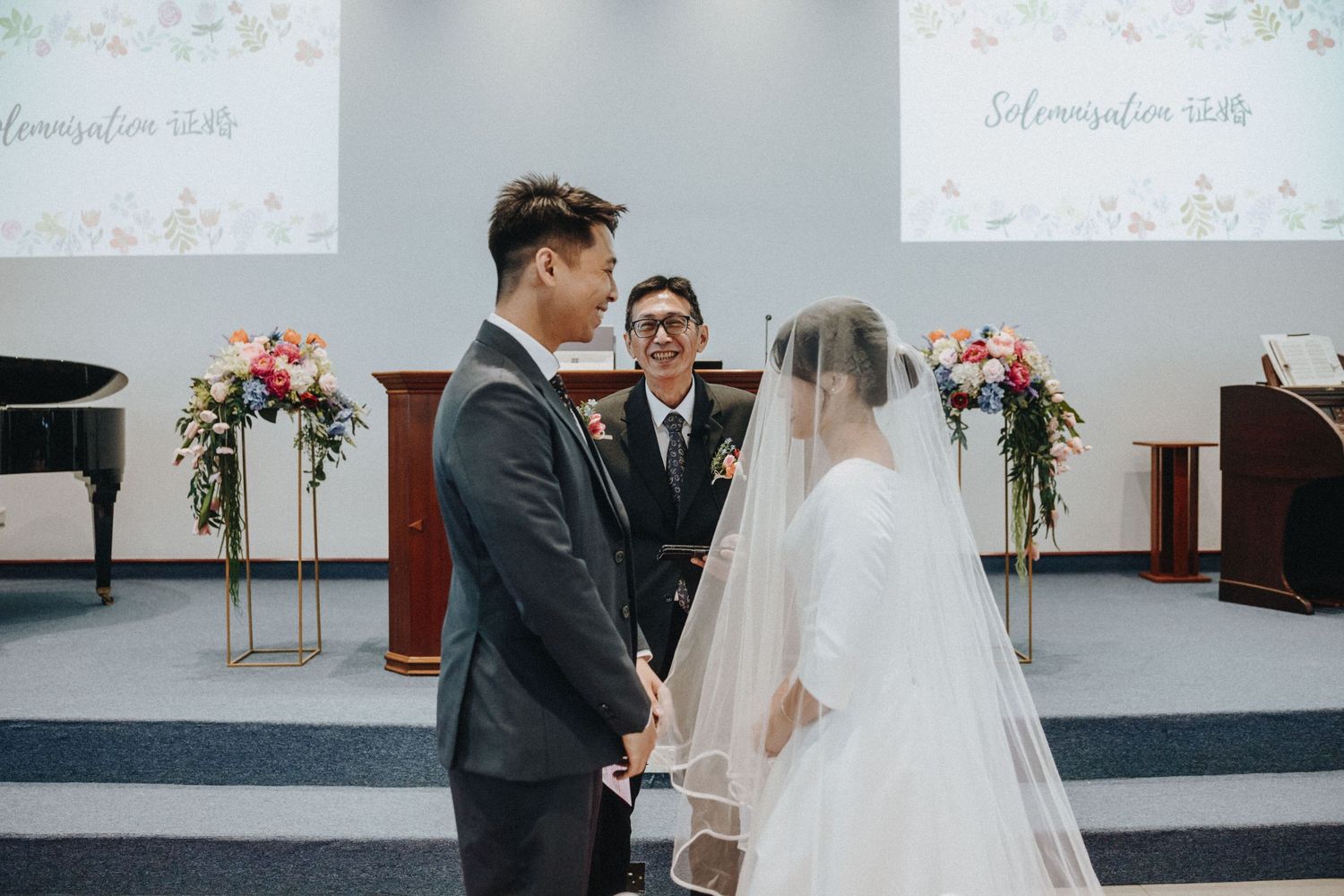 Bride and groom holding hands at the altar during a church wedding ceremony with floral arrangements nearby.
