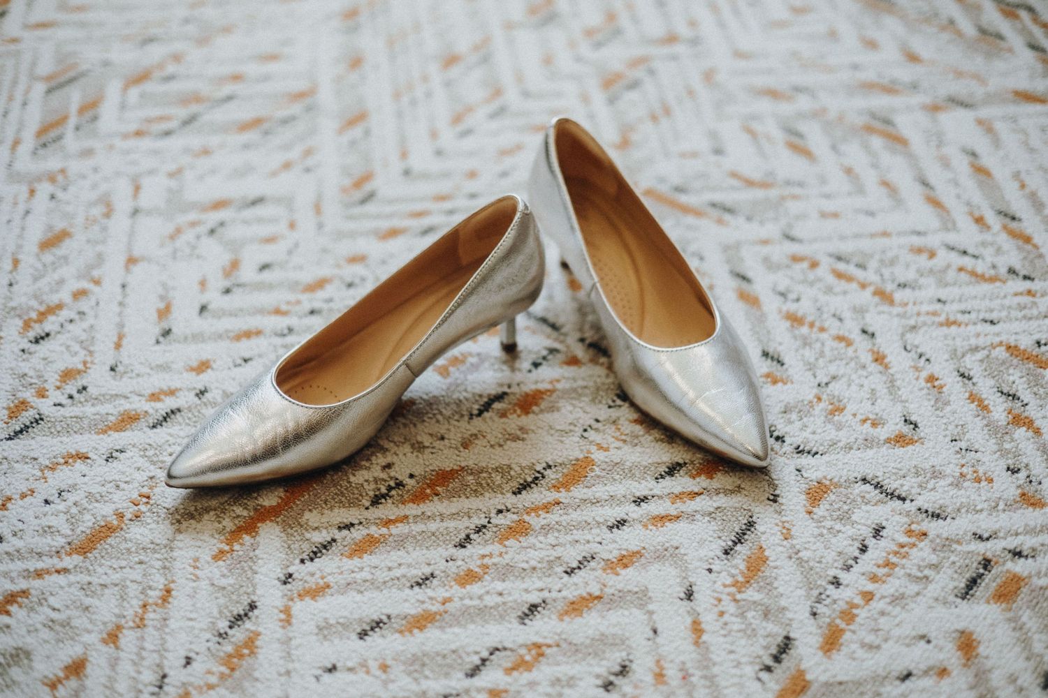 Silver kitten heel pointed-toe pumps displayed on a textured white lace surface for a wedding.