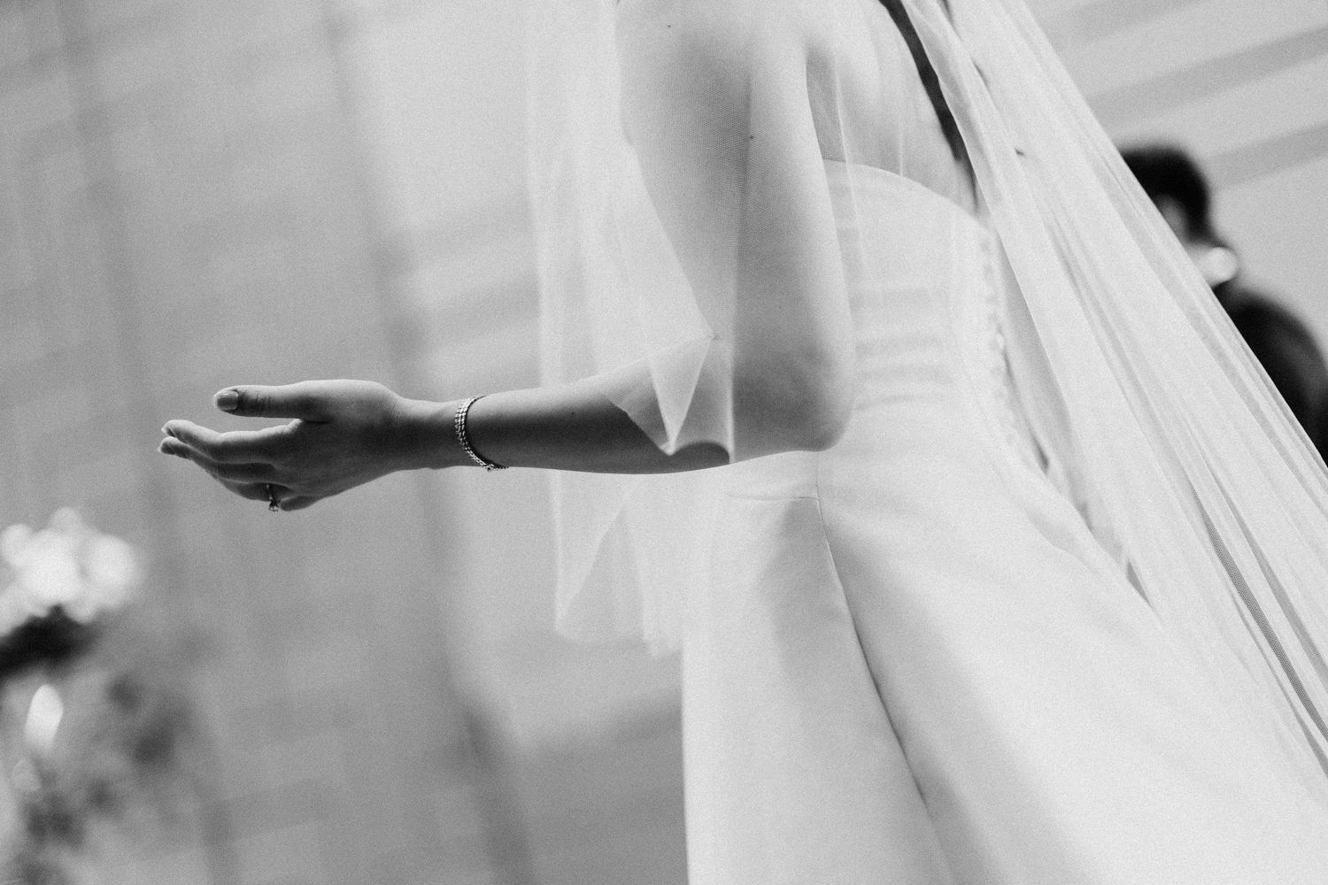 Close-up black and white image of a flowing white wedding veil and outstretched arm.