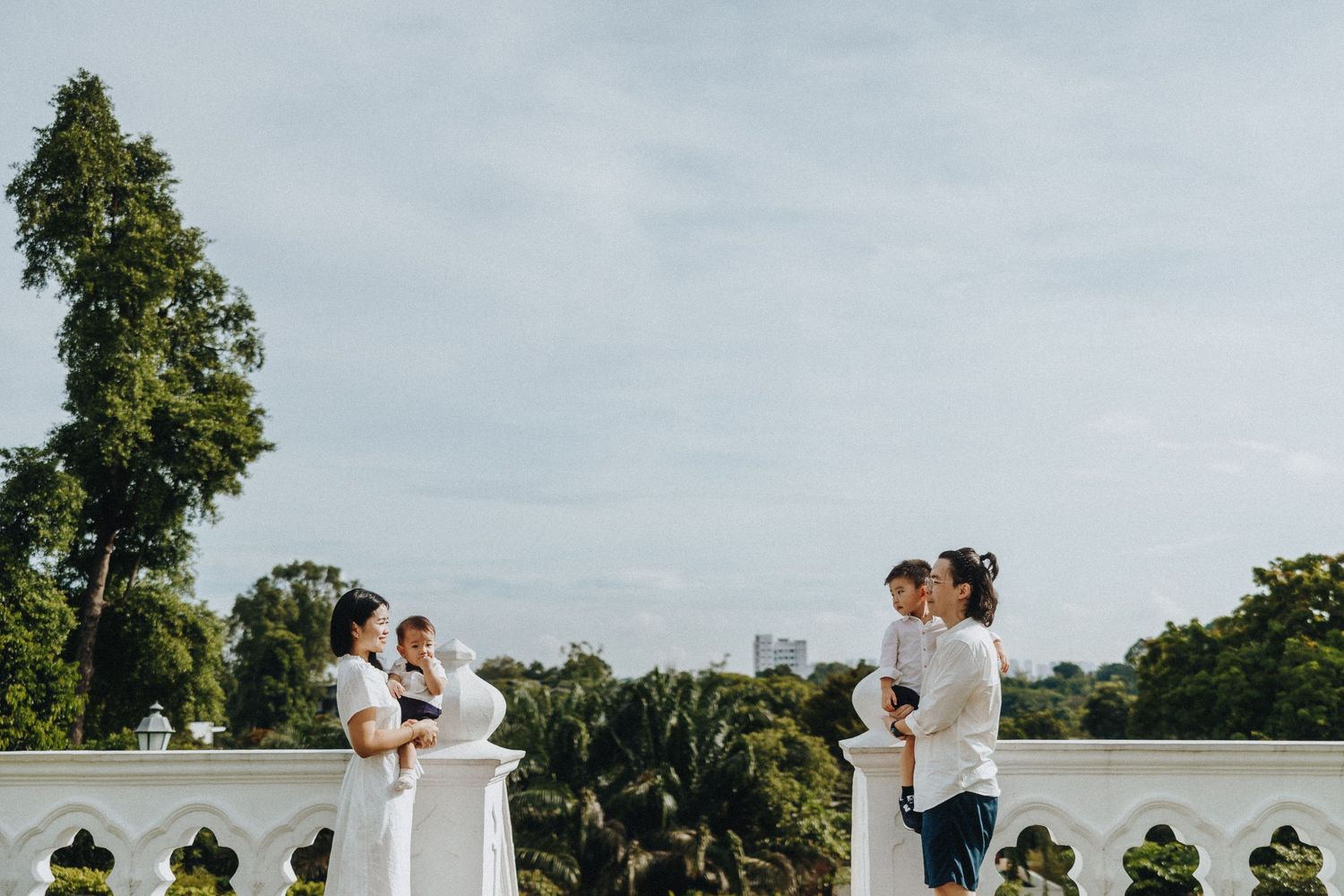 People enjoying conversation on an elegant white terrace overlooking lush greenery on a cloudy day.