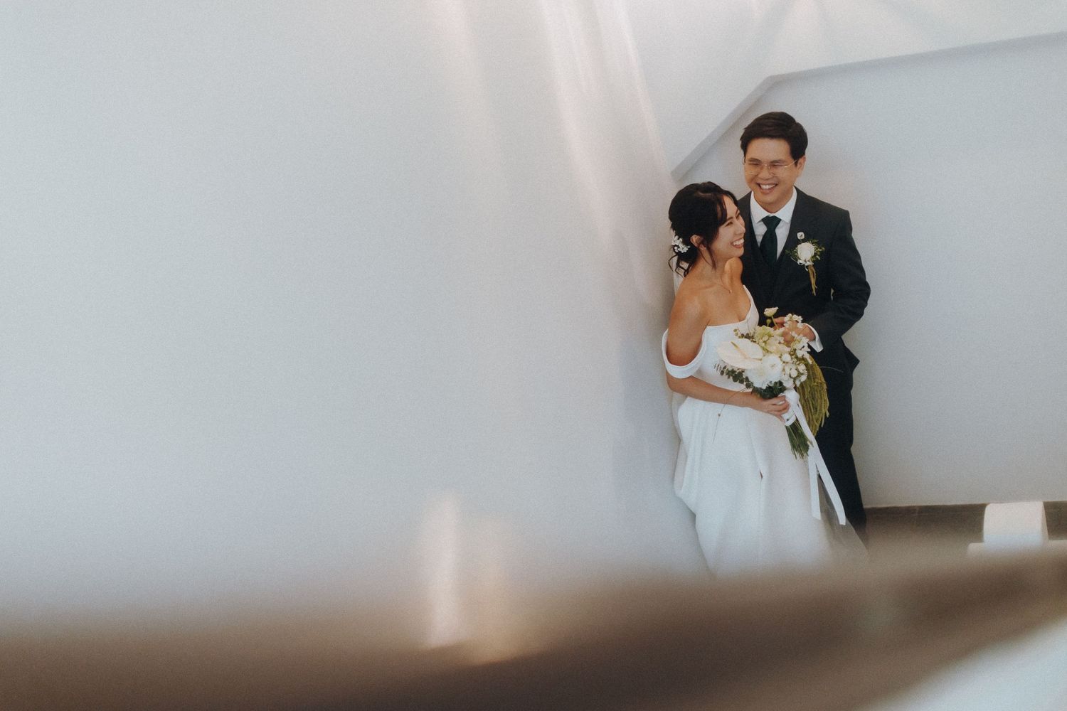 A couple shares an intimate moment during their wedding day against a white minimalist backdrop.