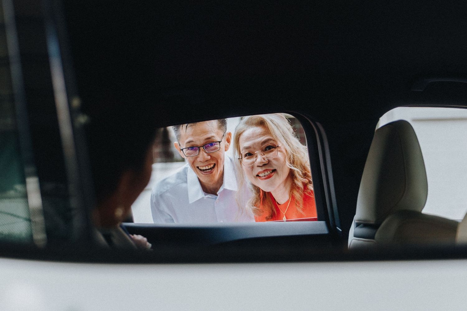 A reflection in a car mirror shows two people smiling through a car window.