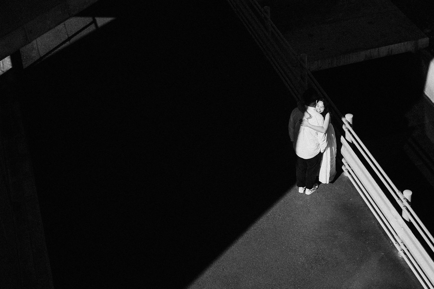 A dramatic black and white photo of two figures standing by a railing at night.