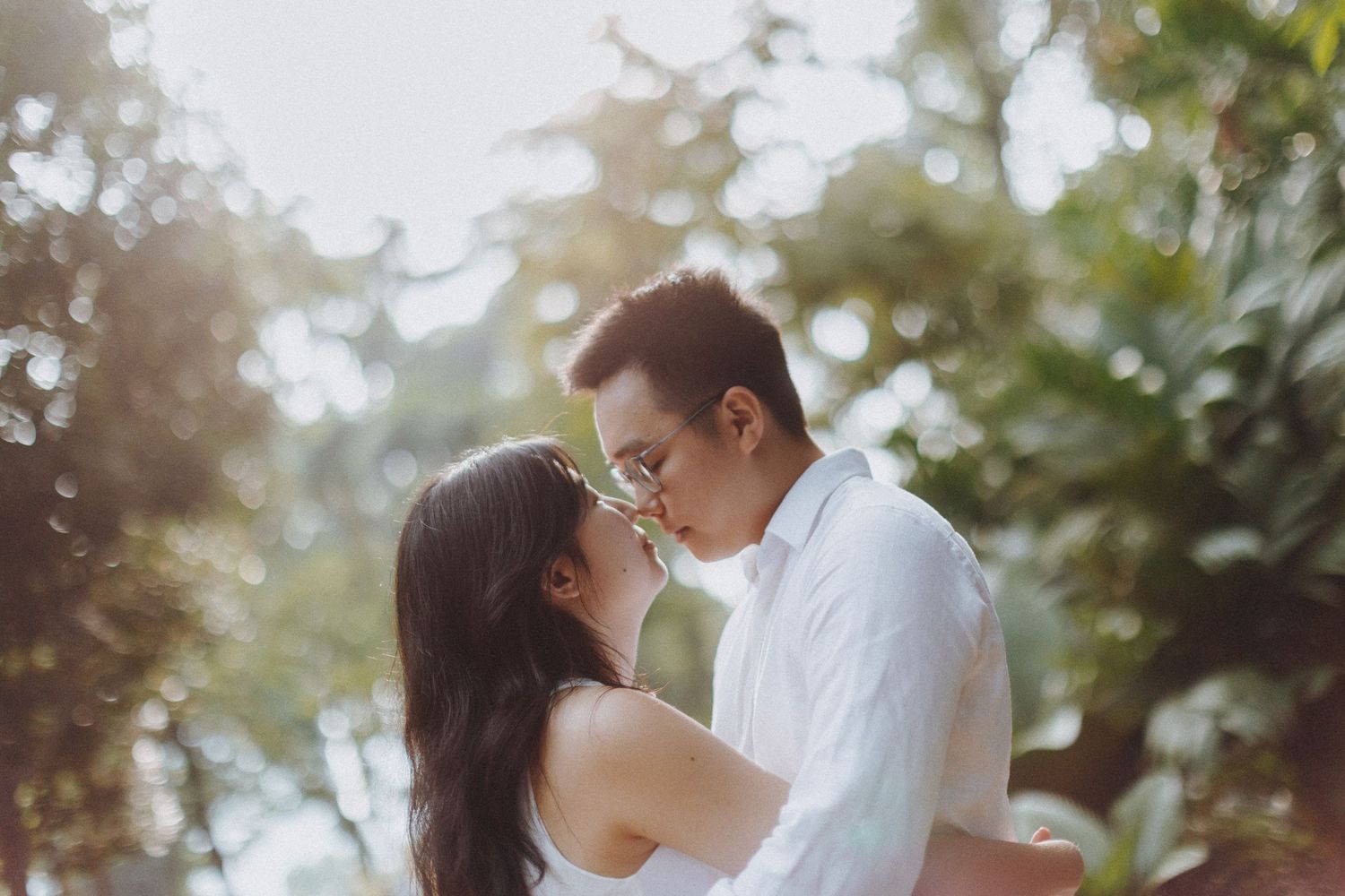 A couple shares an intimate moment embracing in a sunlit garden with lush greenery in the background.