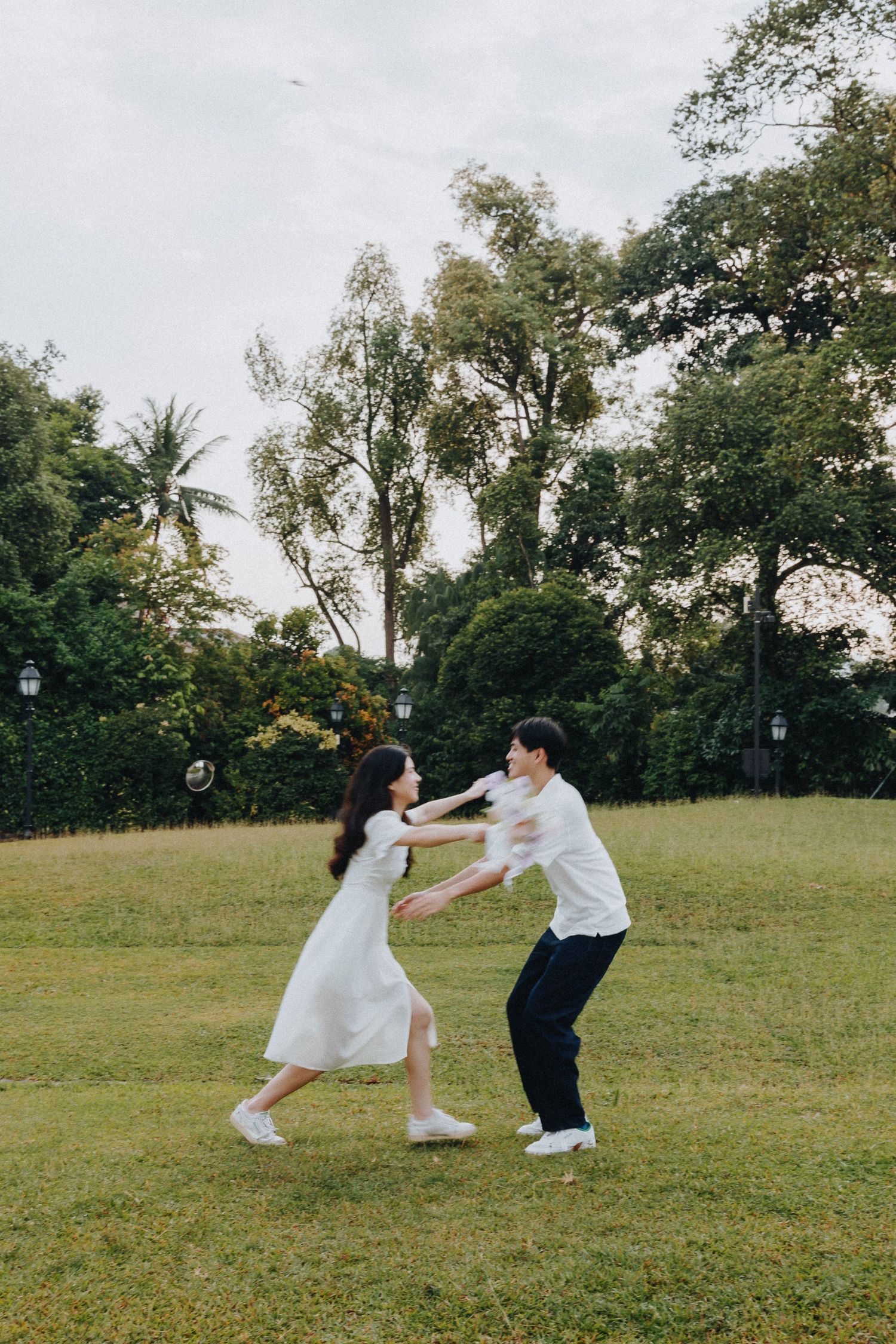 A playful couple in matching white outfits dancing together on a grassy field.