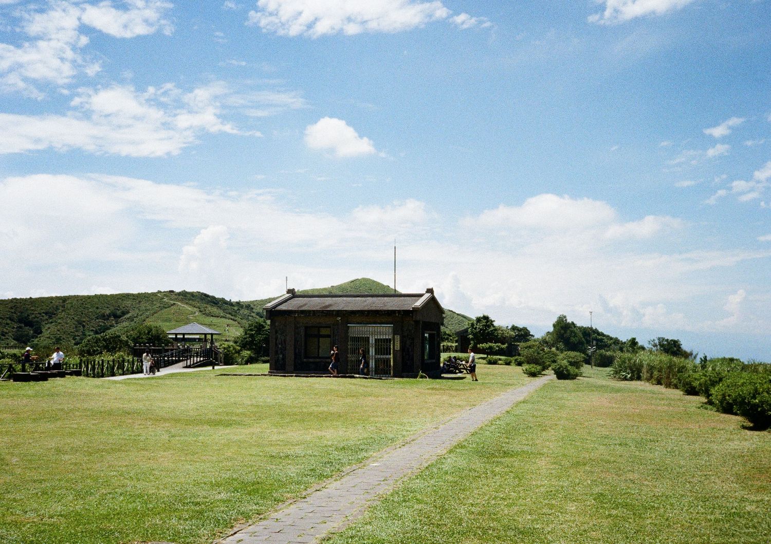 Panoramic view of a green hillside with dirt paths and buildings scattered across the landscape.
