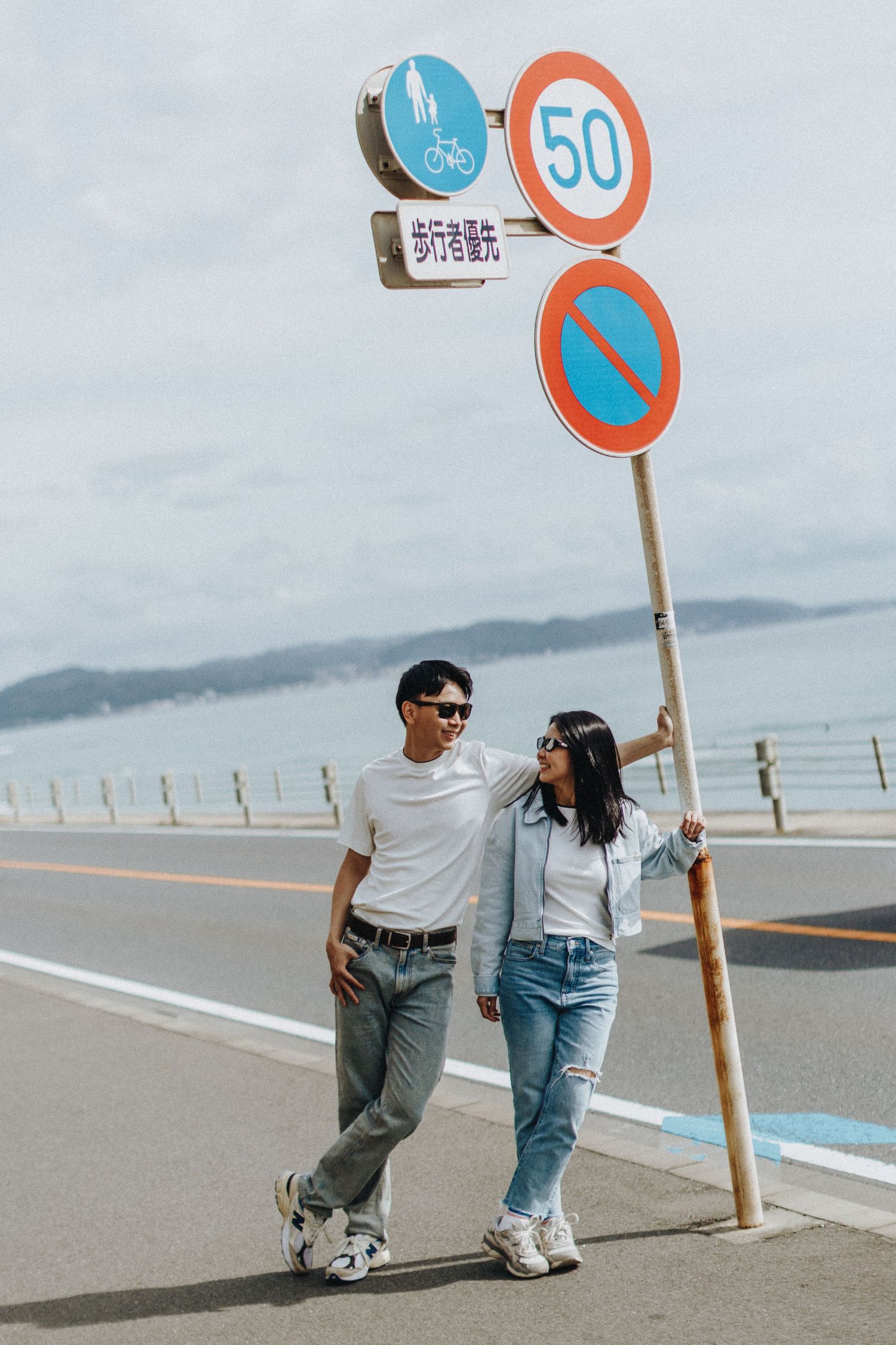 Traffic signs and poles line a coastal road with mountains visible in the distance.