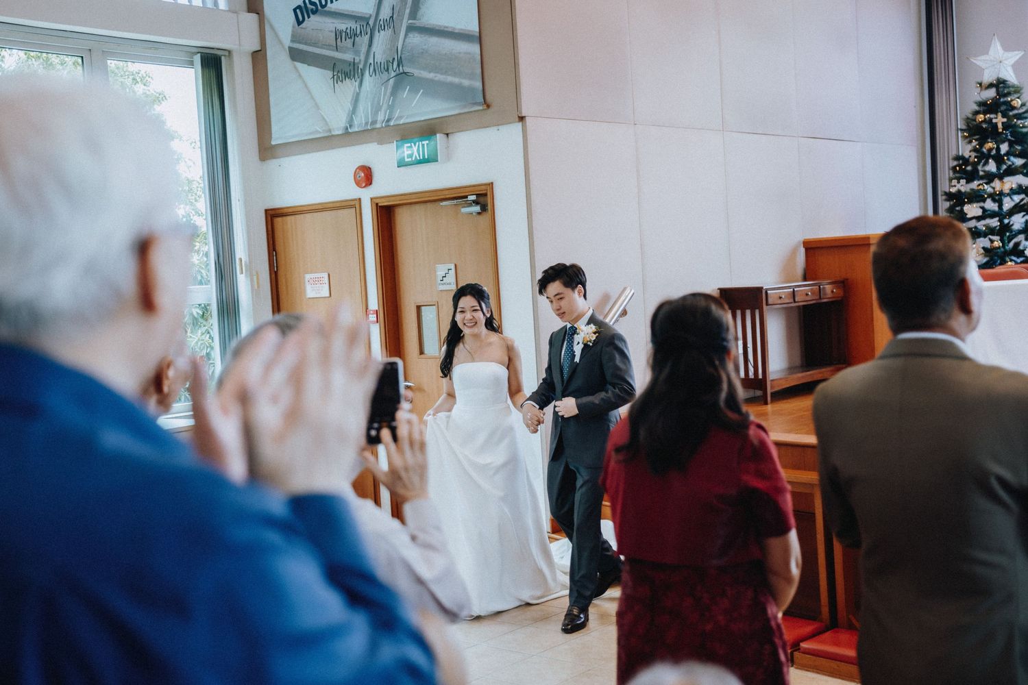 Bride and groom walking down aisle as guests applaud at church wedding.
