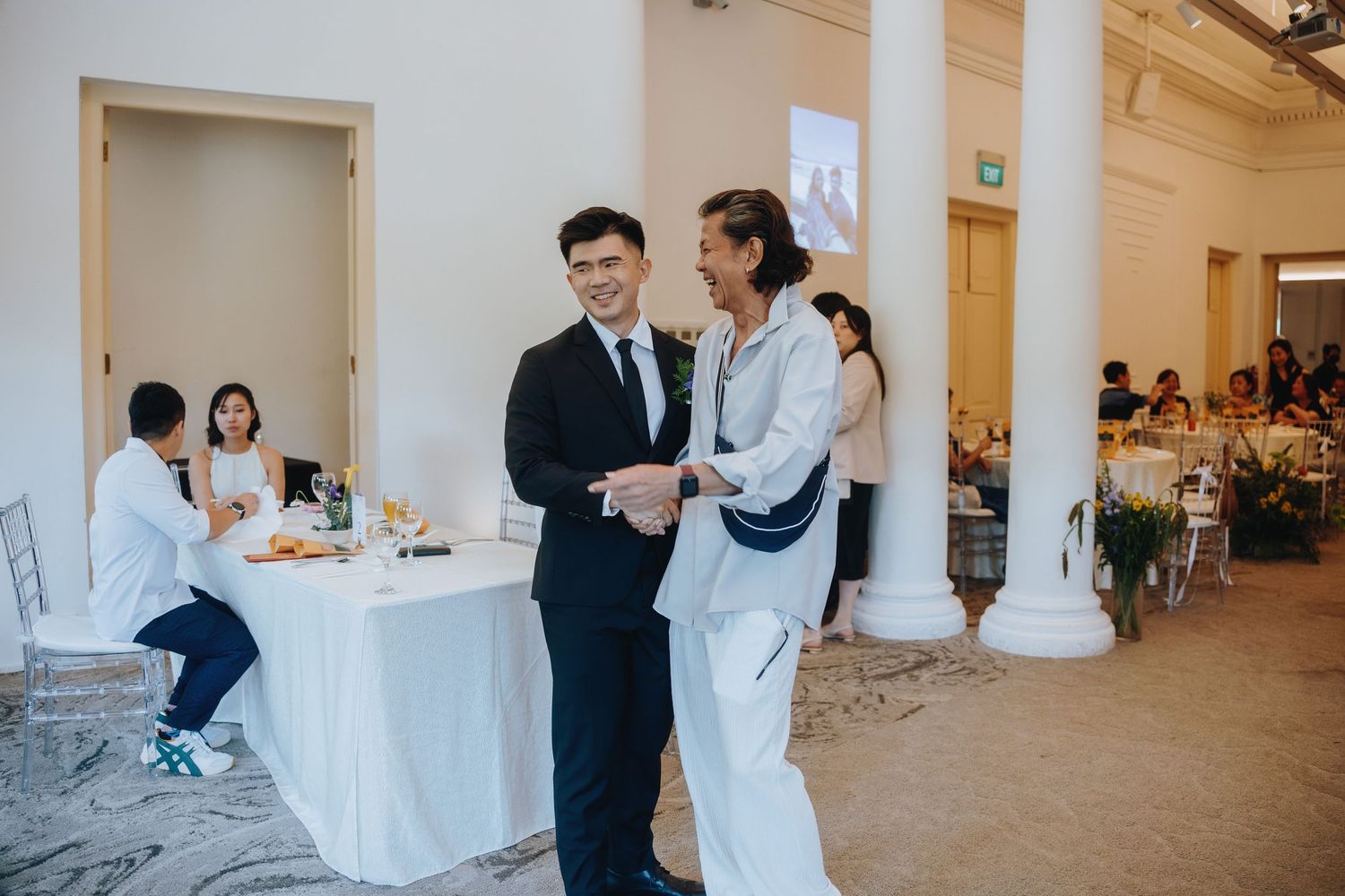 Two men in formal attire smiling and conversing at an elegant wedding reception venue.