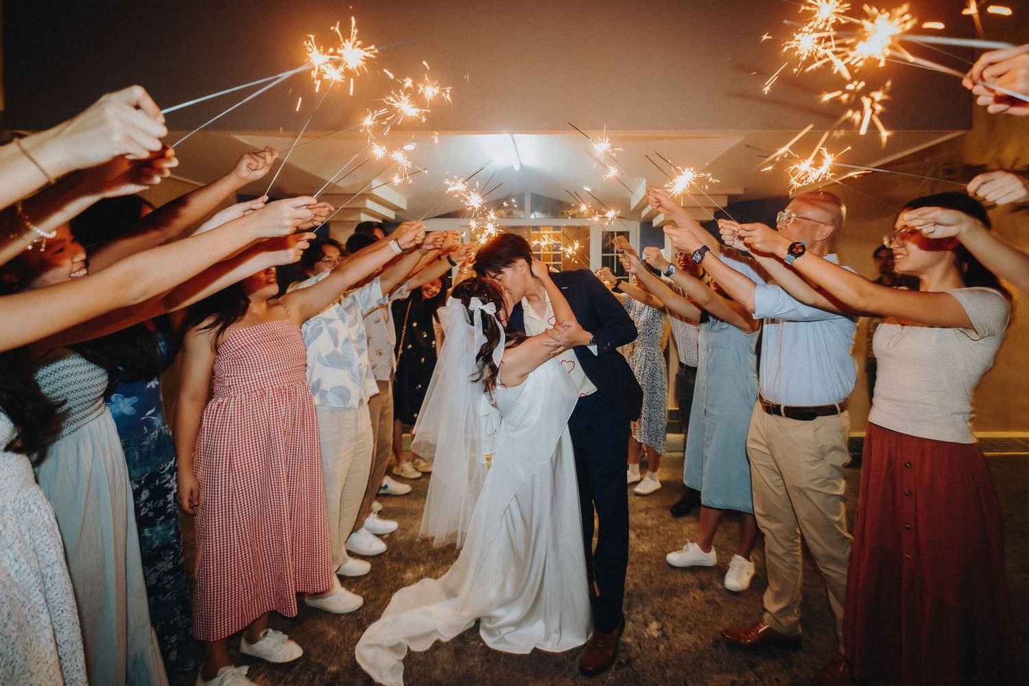 Wedding guests holding sparklers create a magical light tunnel as newlyweds dance through the night at their reception.