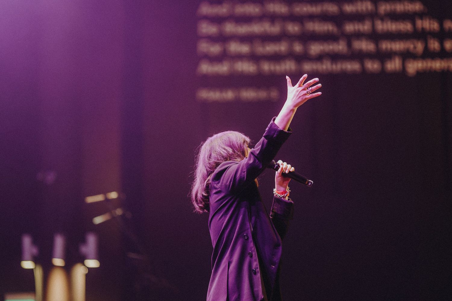 Concert crowd illuminated by purple stage lights creating an atmospheric mood during a live performance.